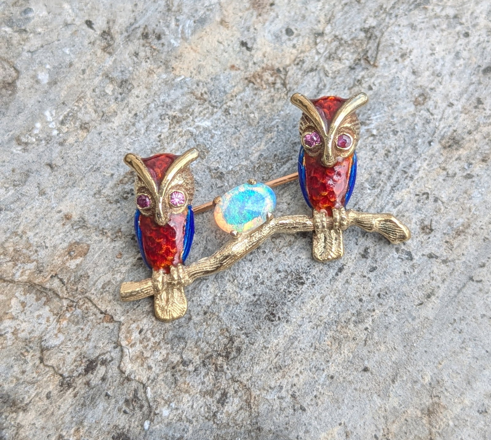 Enamel Owl and Opal Pin: Crafted in 14k yellow gold, The owls display colorful enamel with ruby eyes and (1) opal in the center. The brooch measures 1 1/2in x 1in and weighs 4.2dwt. It is stamped 14k