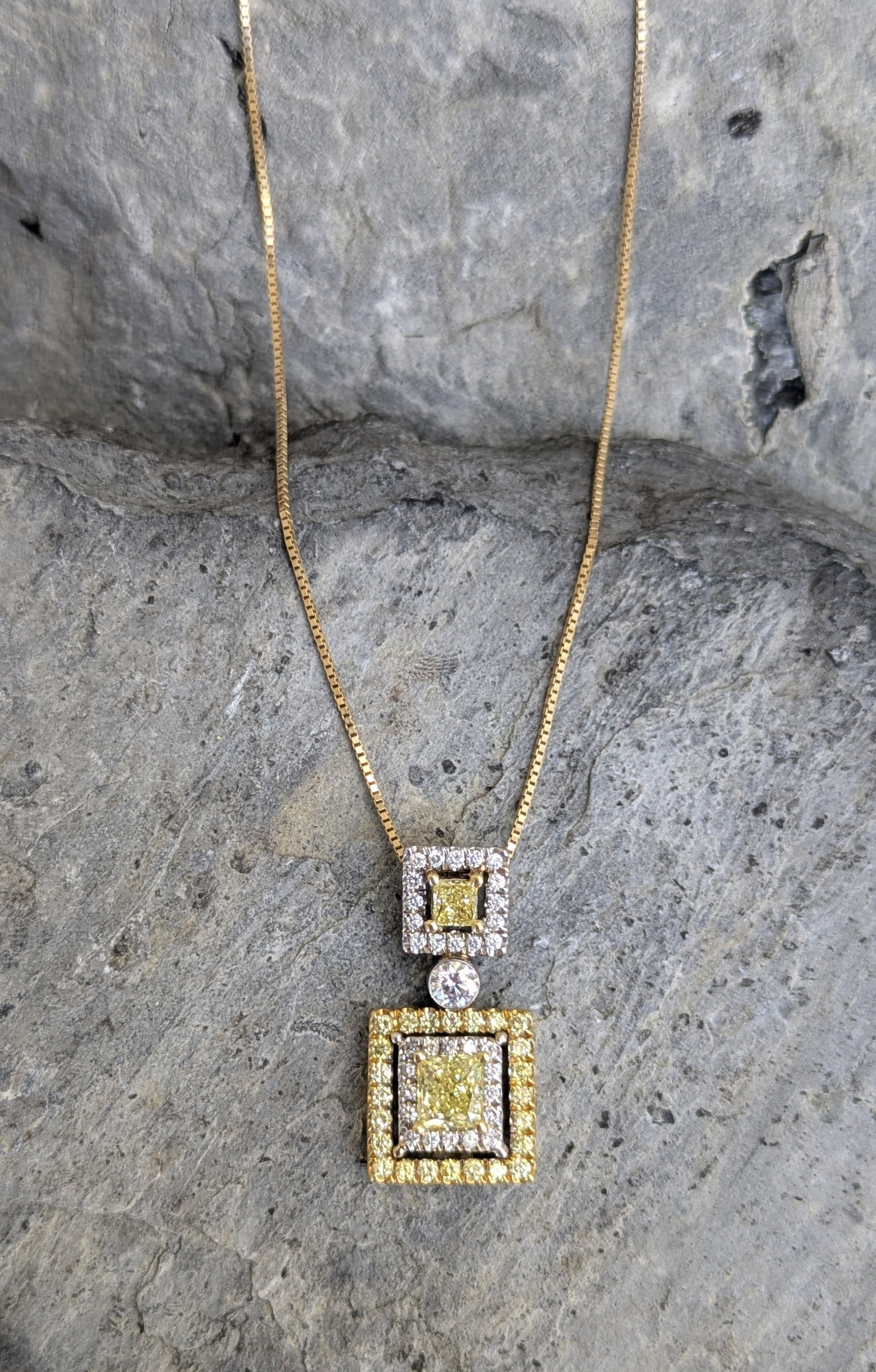 Fancy Yellow Diamond Pendant: Crafted in 18k white and yellow gold, the diamond pendant features (2) princess cut fancy yellow diamonds measuring 5.1mm x 4.8mm x 3.7mm and 3.2mm x 3.5mm x 2.1mm respectively. The total weight of th