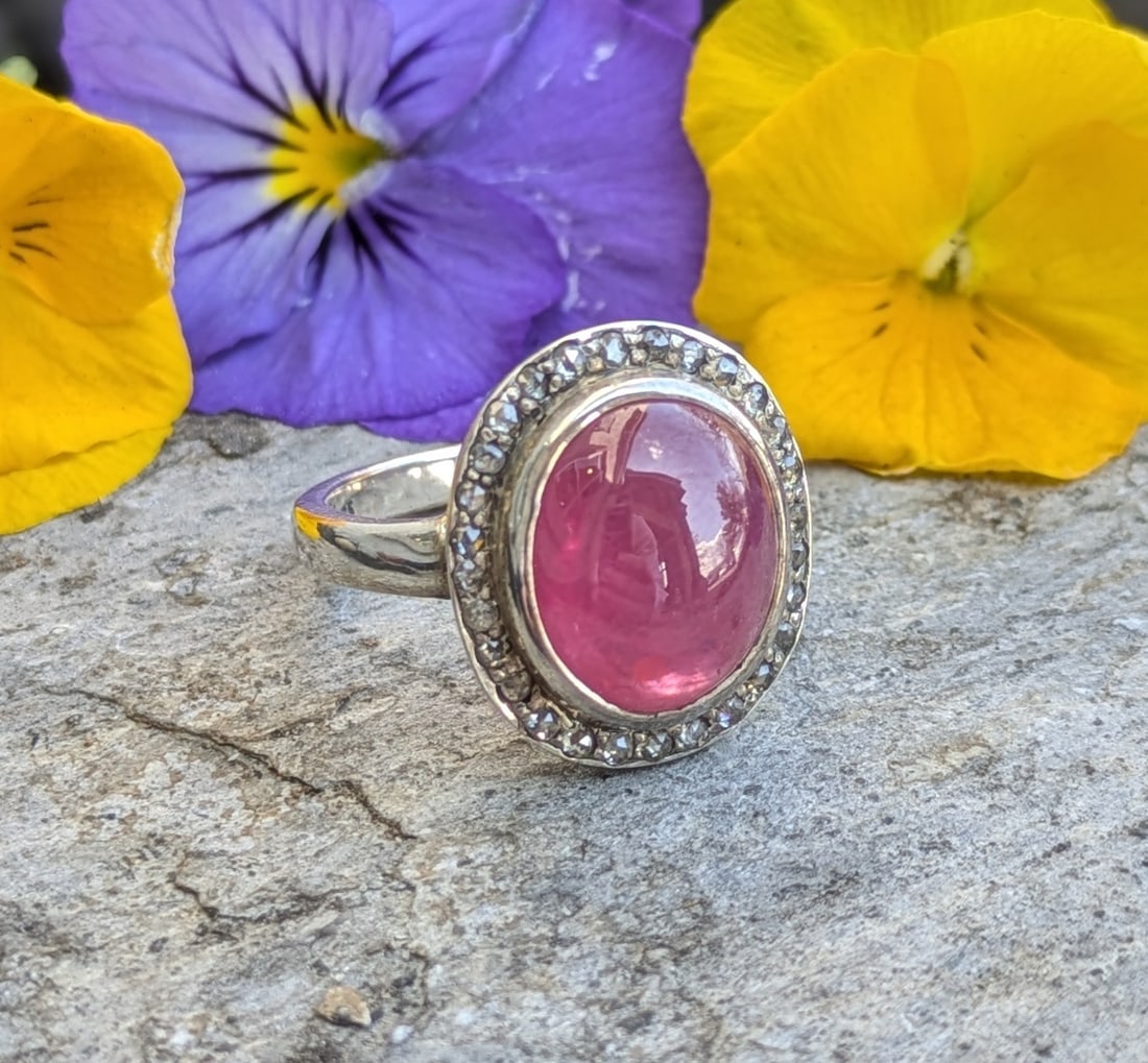 Vintage Ruby and Diamond Ring: Crafted in sterling silver featuring (1) cabochon ruby measuring 12mm x 10.2mm x 5.8mm and weighing approximately 7.71ct. Surrounding the ruby, there are (28) old mine cut diamonds weighing approximat