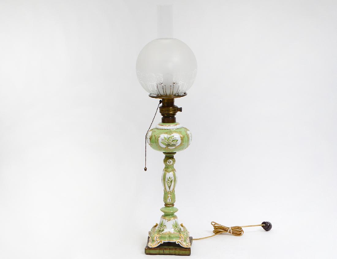 ROCOCO STYLE FOLIATE DECORATED PORCELAIN OIL LAMP: 20th Century. Probably English. The reservoir, stem and base reserved with foliage, on a light green ground, electrified. (Cond: good) (150/200)