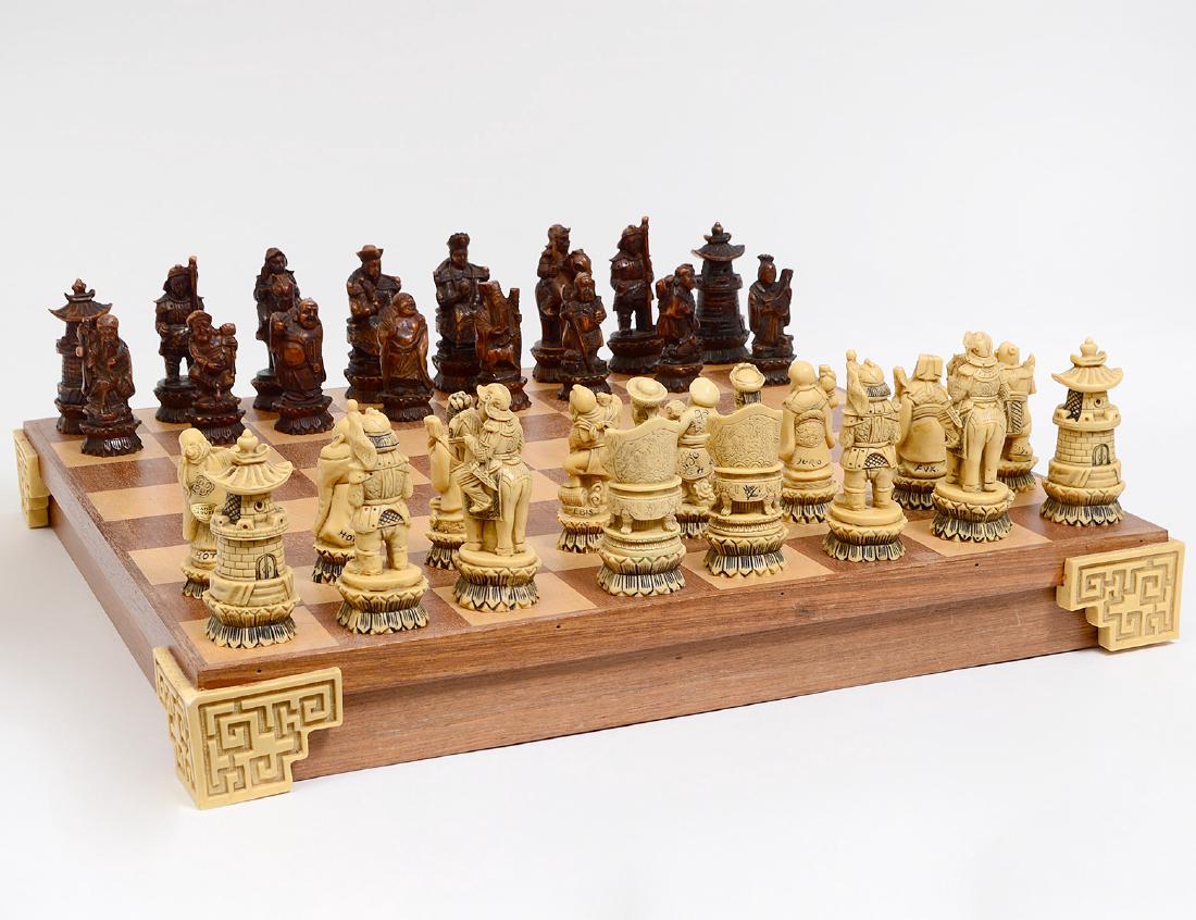 CHINESE CARVED COMPOSITION CHESS SET & BOARD: Modern. Stained brown and white, carved to represent An Emperor and Empress, merchants, sages, warriors and nobles, boxed with the lid serving as the chessboard. Height of tallest piece 4”. Board 20