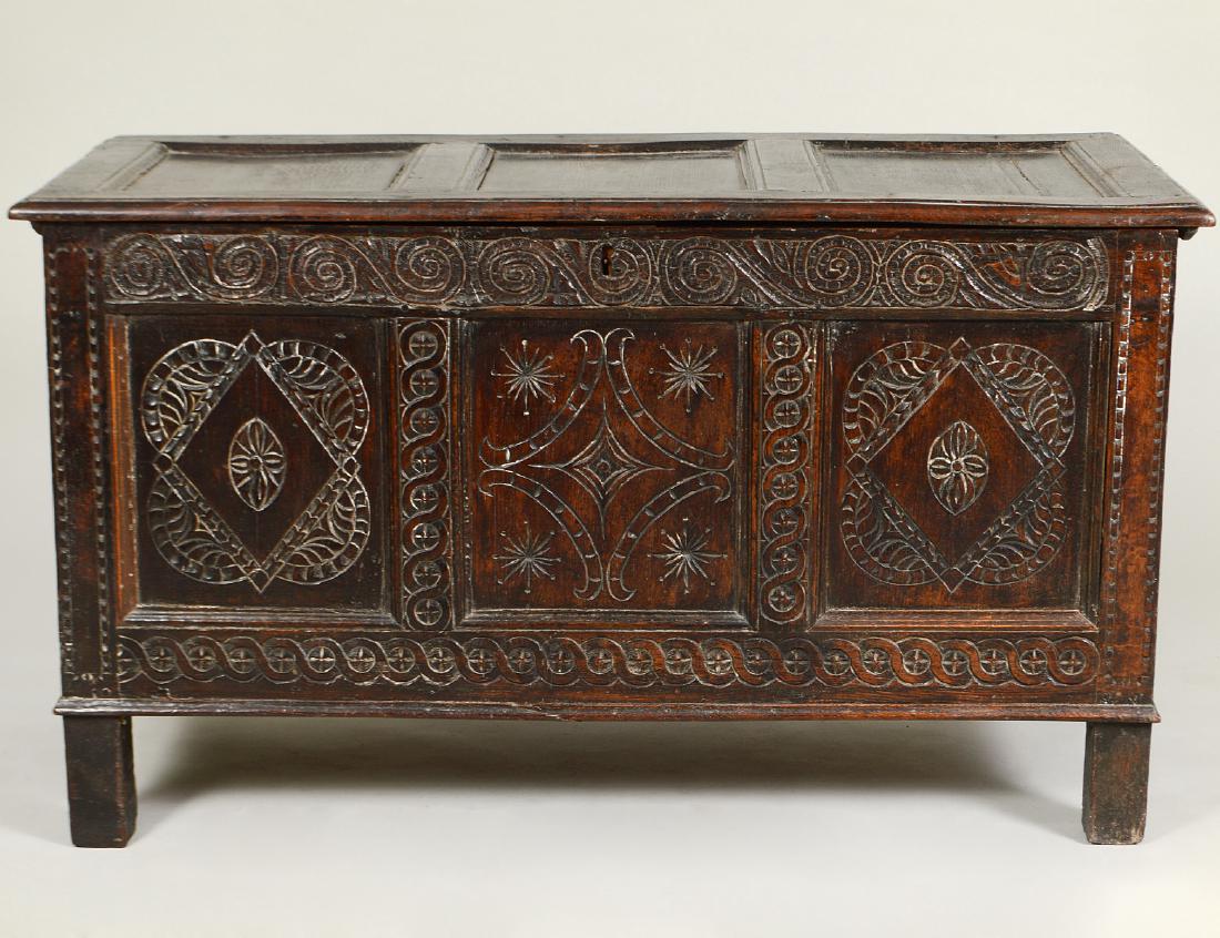 STUART CARVED OAK COFFER: English. Circa 1650. The hinged rectangular panel inset top, above a façade with geometric carved inset panels within a carved upper and lower border, the sides with panel insets, on later pain block