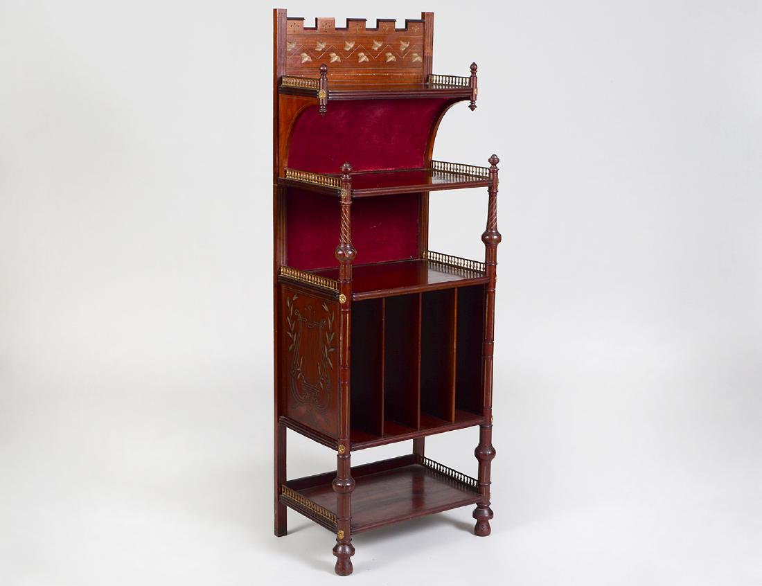 ENGLISH EASTLAKE MAHOGANY SHELVED MUSIC STAND: Circa 1900. Carved with various motifs, with brass galleries, open shelves and slots for sheet music, on turned legs, ending in casters. Height 54 ½”. Width 19”. Depth 13 ¼”. (Cond: lacking tw