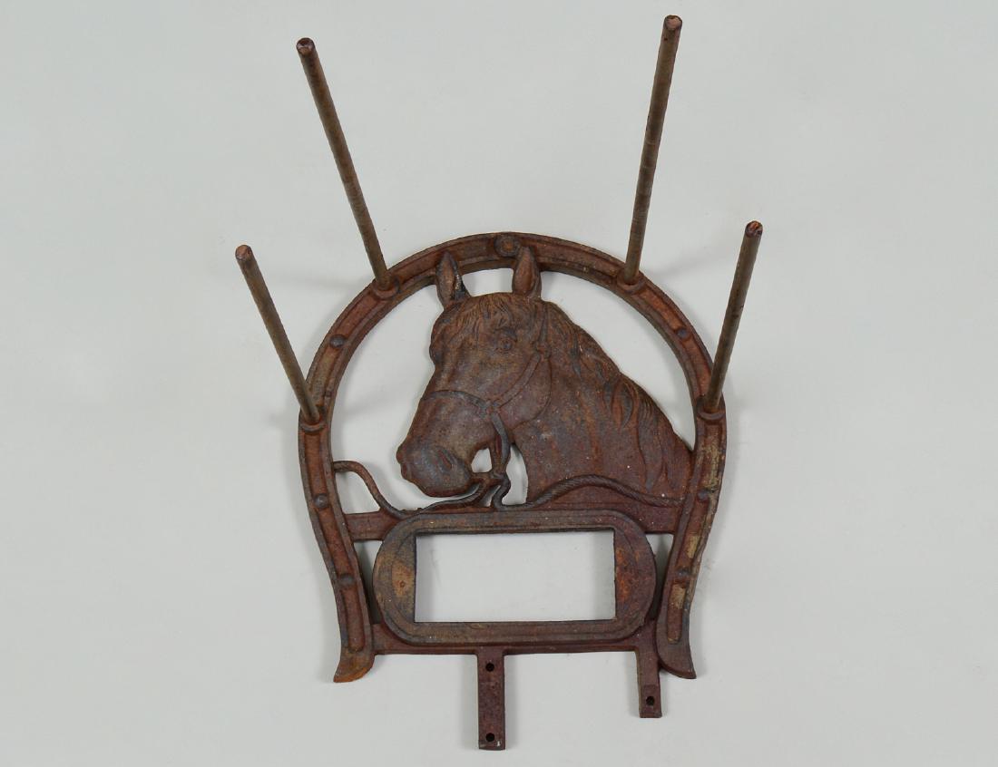 IRON HORSESHOE FORM STABLE BRIDAL RACK: American/English. Circa 1900. Further cast with a horse head, and rectangular opening for a name plaque, with long projecting rods. Height 17 ½”. Width 14”. Depth 16 ½”. (Cond: oxidized) (250/
