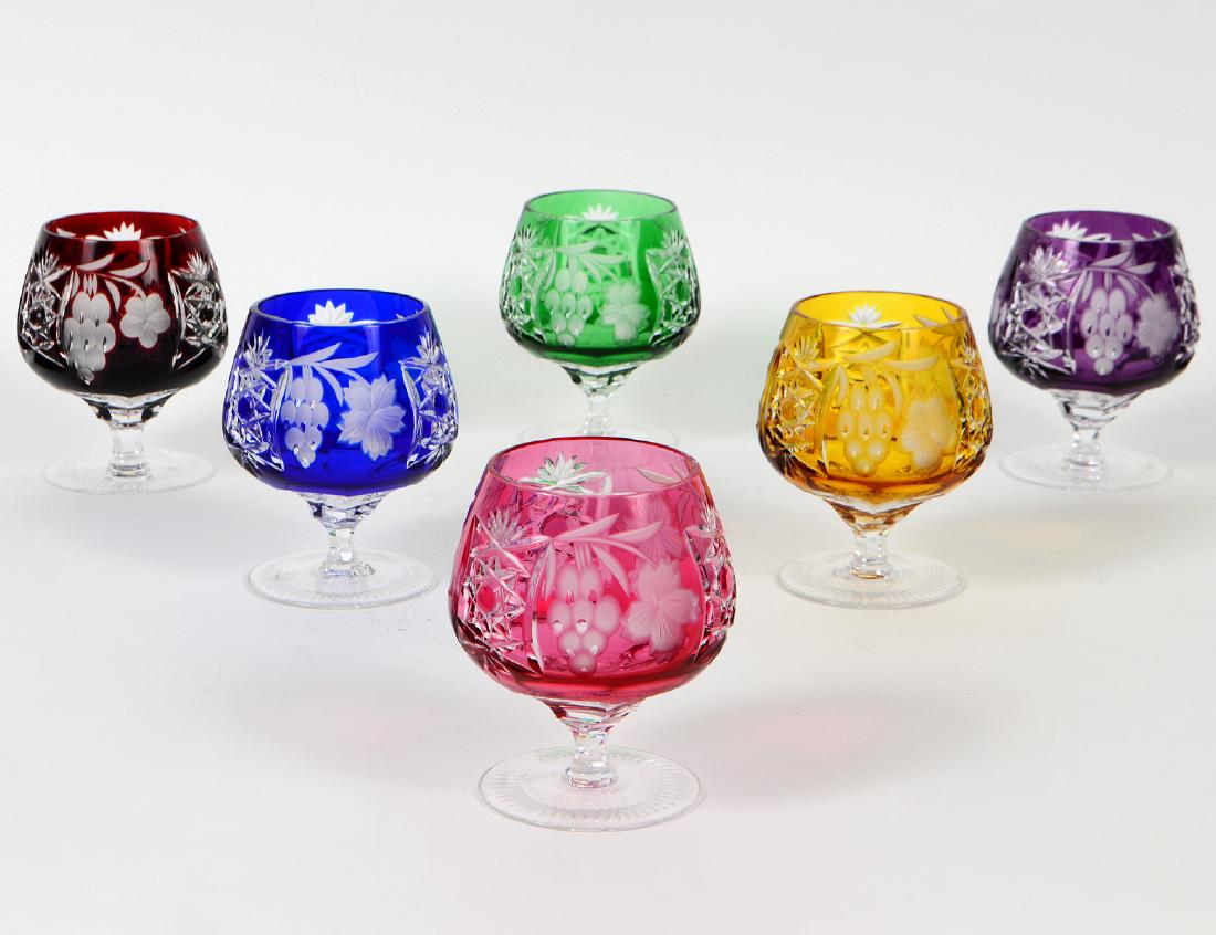 SIX VARIOUSLY COLORED CUT GLASS GOBLETS: Each cup shaped bowl cut with stars and etched with foliage, on short stems, with circular feet. Height 4 Â½Â”. Diameter at opening 2Â”. (100/150)