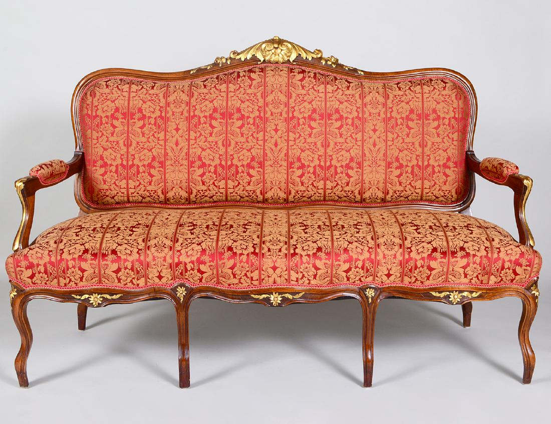 LOUIS XV STYLE PARCEL GTILT CARVED WALNUT SETTEE: The padded serpentine back with a center gilt foliate crest, with padded arms, centering a serpentine seat, on cabriole legs. Height back to floor 42". Length 5’1". (Cond: good)