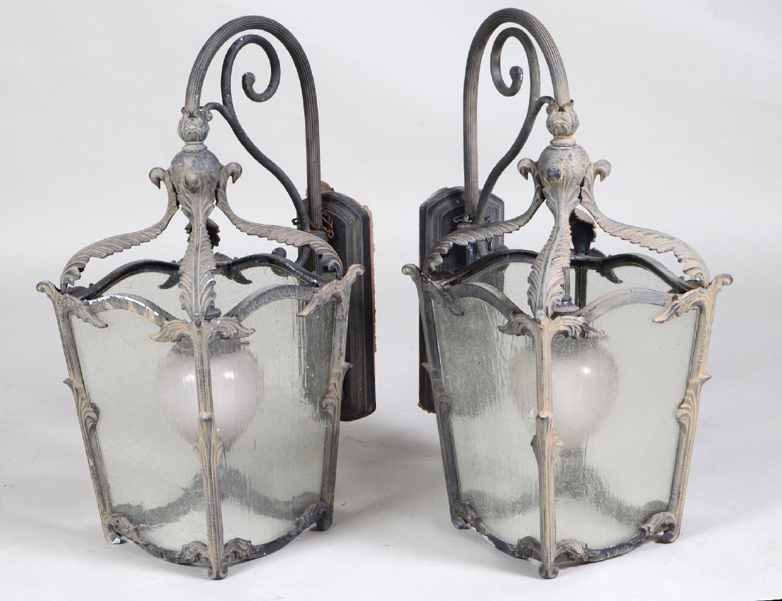 PAIR OF PATINATED METAL & GLASS COACH LANTERNS: Each with four glazed sides, beneath leaf clasps, with a single center pendant light, hung from a scroll, with wall plate. Height 27". Width 16". (Cond: good)