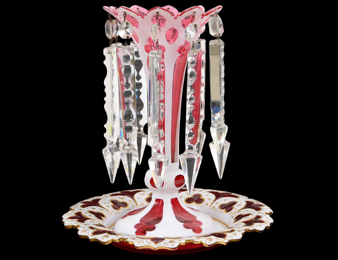BOHEMIAN WHITE CUT TO RED GLASS VASE & UNDERPLATE: Circa 1900. The trumpet form vessel hung with prisms, the circular scallop cut plate with gilt highlights. Height of vase 10 1/4". Diameter of plate 9". (Cond: good, one prism detached)