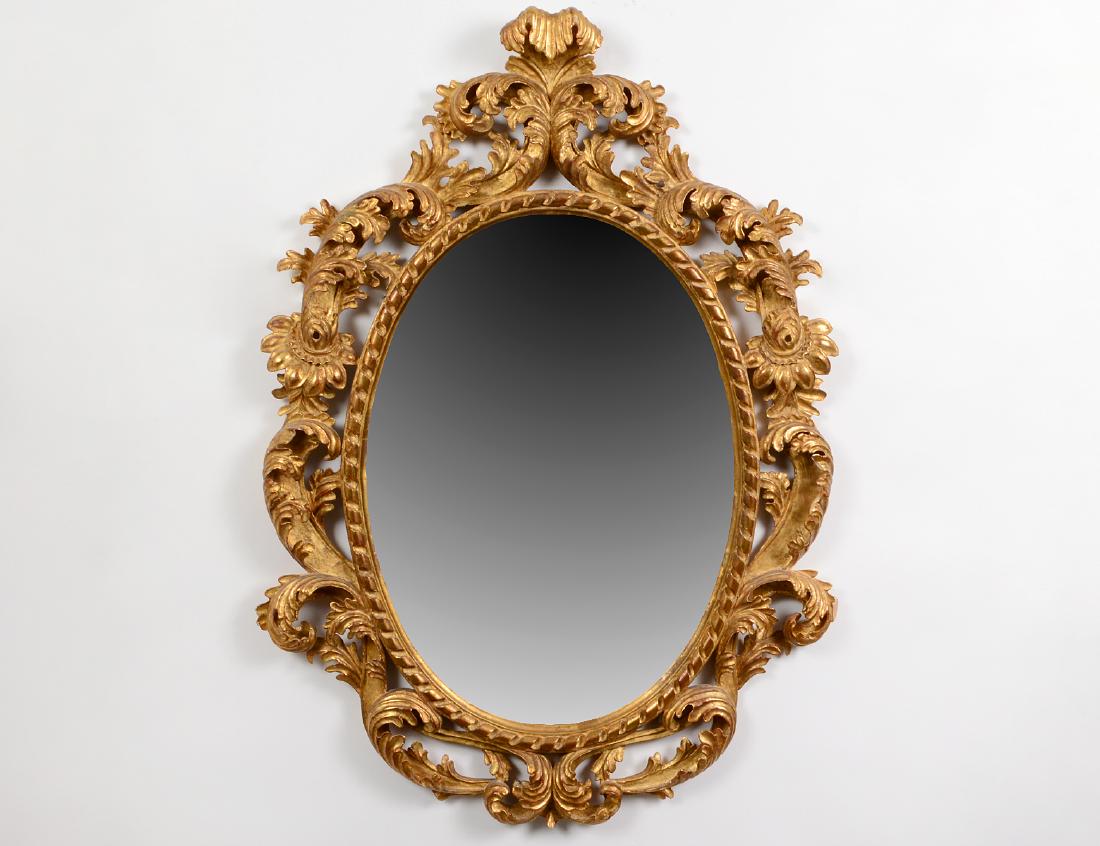 ROCOCO STYLE GILTWOOD OVAL MIRROR: The beveled mirror plate, with a twist border, with bold scrolls all around. Height 43". Width 31". (Cond: good, one leaf repaired)