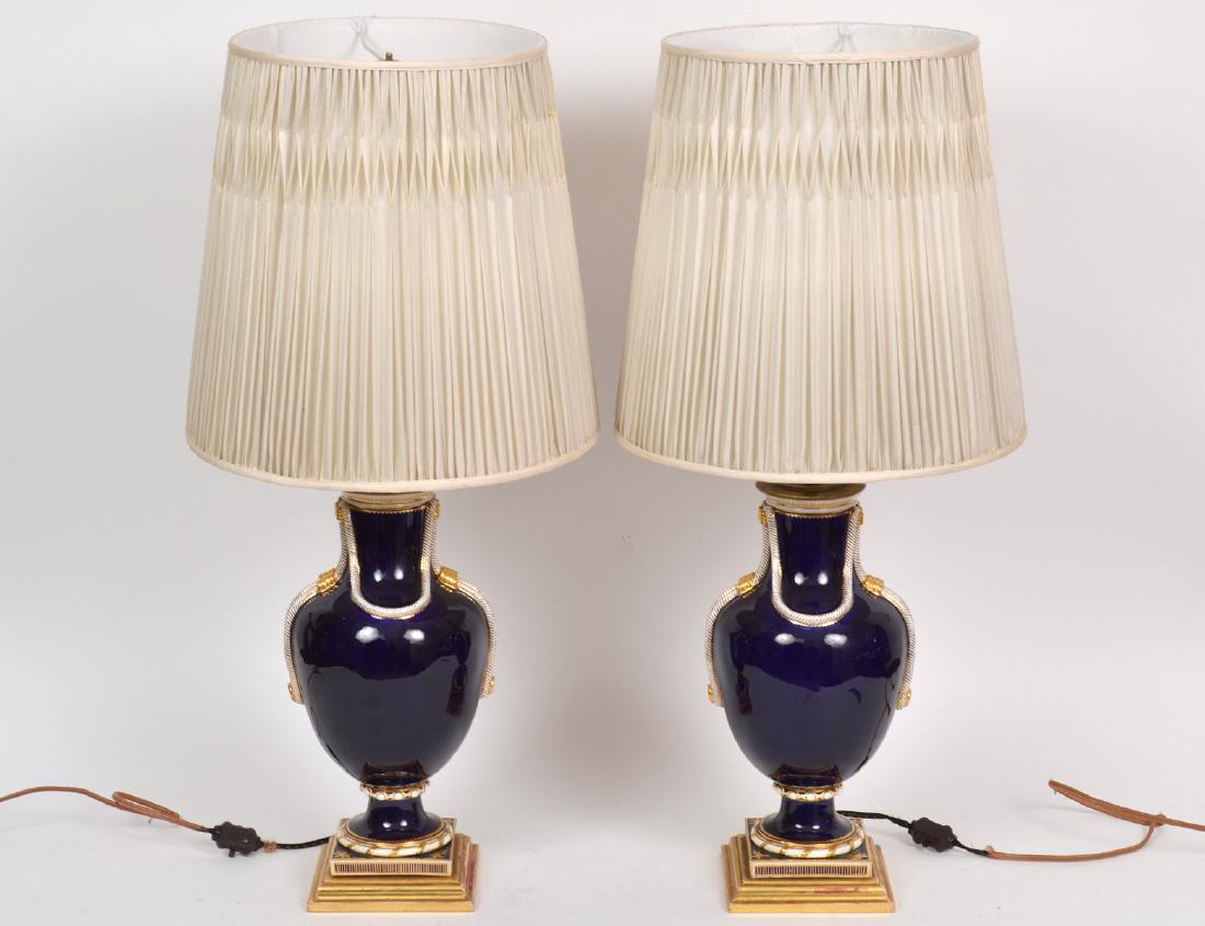 PAIR OF GERMAN COBALT GROUND PORCELAIN LAMPS: 20th Century. Each urn form body with pendant looped rope motifs, on square bases with overall gilt highlights, drilled, fitted for electricity. Height 13 1/2". (Cond: good) PROVENANCE: From The Colle