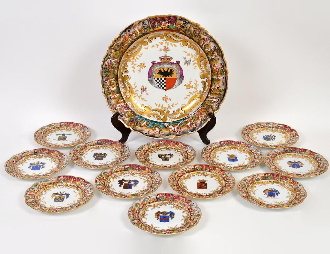 CAPODIMONTE ARMORIAL PORCELAIN CHARGER & TWELVE PLATES: Early 20th Century. The underside marked. The center recesses with armorials, with an outer rim of raised foliage, gilt scrolls, and frolicking putti. The plates with varying armorials. Diameter of ch