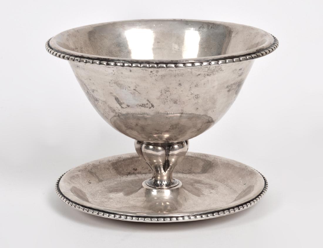 GEORG JENSEN SILVER BOWL ON STAND: Early 20th Century. Underside marked 830 S, Georg Jensen, 1919, with other markings. The circular tapering hand-hammered bowl with beaded edge above a lobed tapered stem affixed to a conforming circul