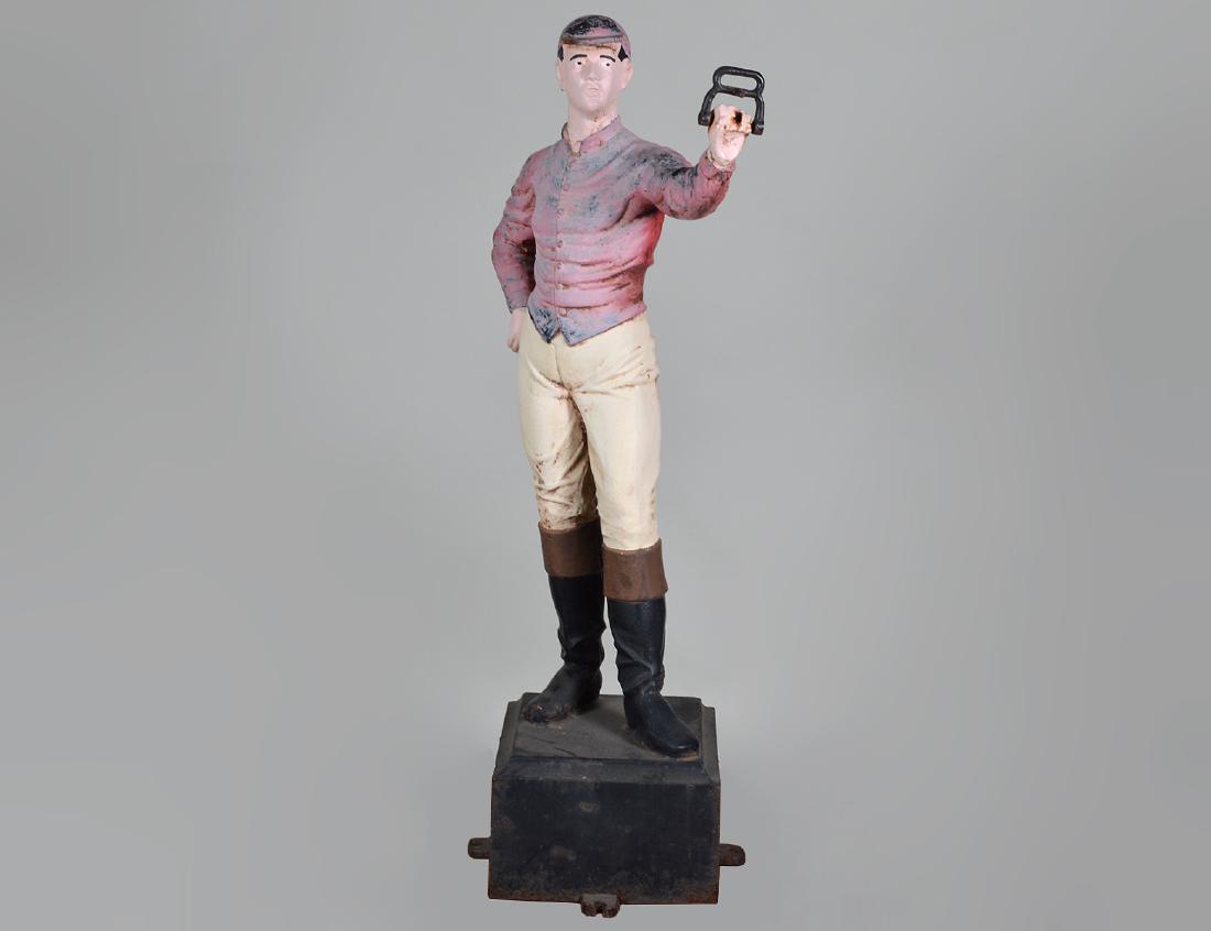 AMERICAN PAINTED CAST IRON LAWN JOCKEY: 20th Century. Appears unmarked, possibly Robert Woods, Philadelphia. Standing in a typical pose with one arm outstretched, presumably for hitching a horse, on a square plinth. Height 49”. (Cond:
