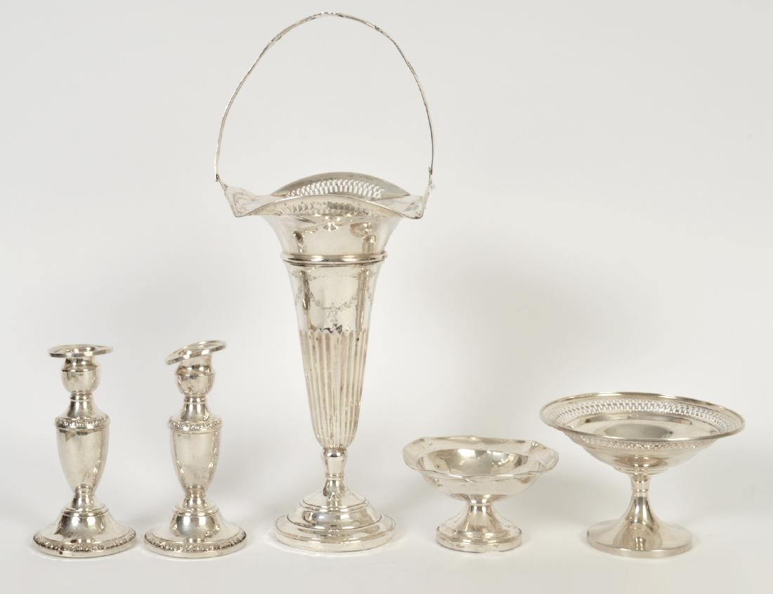 FIVE STERLING SILVER TABLE ITEMS: 20th Century. American, marked. Comprising: a vase with a pierced rim and swing handle, a pair of Rogers candlesticks, a pierced tazza, and a footed bowl, all weighted. Height of vase 10 ½”