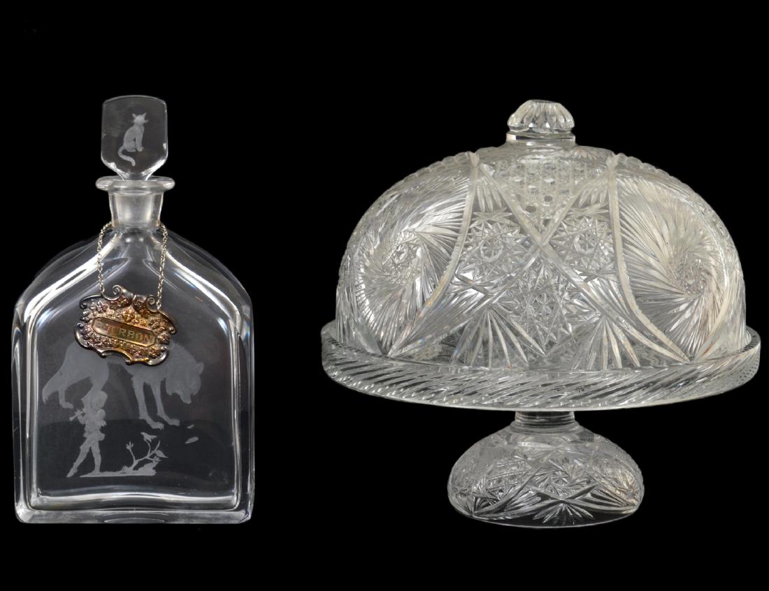 AMERICAN CUT GLASS CAKE DOME ON STAND & A DECANTER: The first, circa 1920, cut with hobnails, stars and flutes; the second with stopper and a silver plate bourbon label, the stopper etched with a cat, the body with a wolf. Height of first 10”. Di