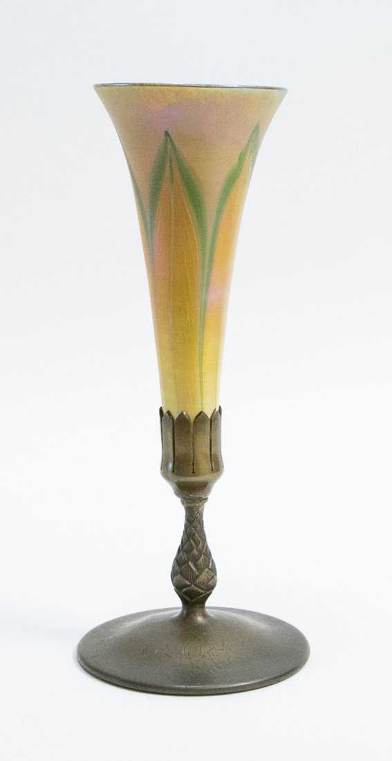 TIFFANY FEATHER DECORATED GLASS AND BRONZE VASE: Circa 1890. The trumpet-form green and white feathered glass upper part, marked L.C.T., set into a bronze base with a circular foot, monogrammed, the underside marked Tiffany Studios, New York, number