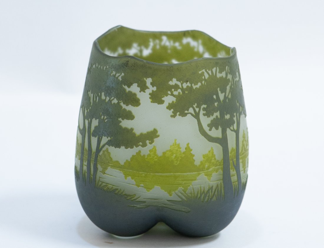 DAUM CAMEO CUT GLASS LANDSCAPE VASE: French. Circa 1900. Signed Daum Nancy. The asymmetrical scalloped rim above a simple flared body, cut all around with grasses and trees before a lake or river in green on a frosted ground, possibly re