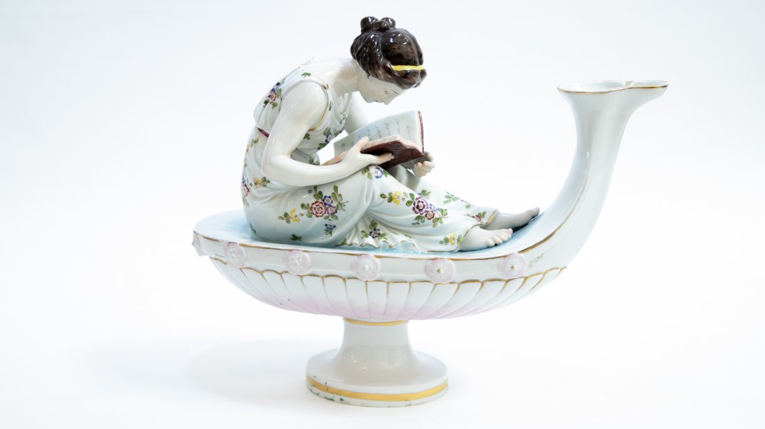 CAPODIMONTE PORCELAIN FIGURAL LADY ON LAMP: Early 20th Century. The crowned N in under glaze blue on the underside. In the form of maiden with a gown decorated with flowers, reading a tome and seated upon an oil lamp, gilt highlights. Height 12