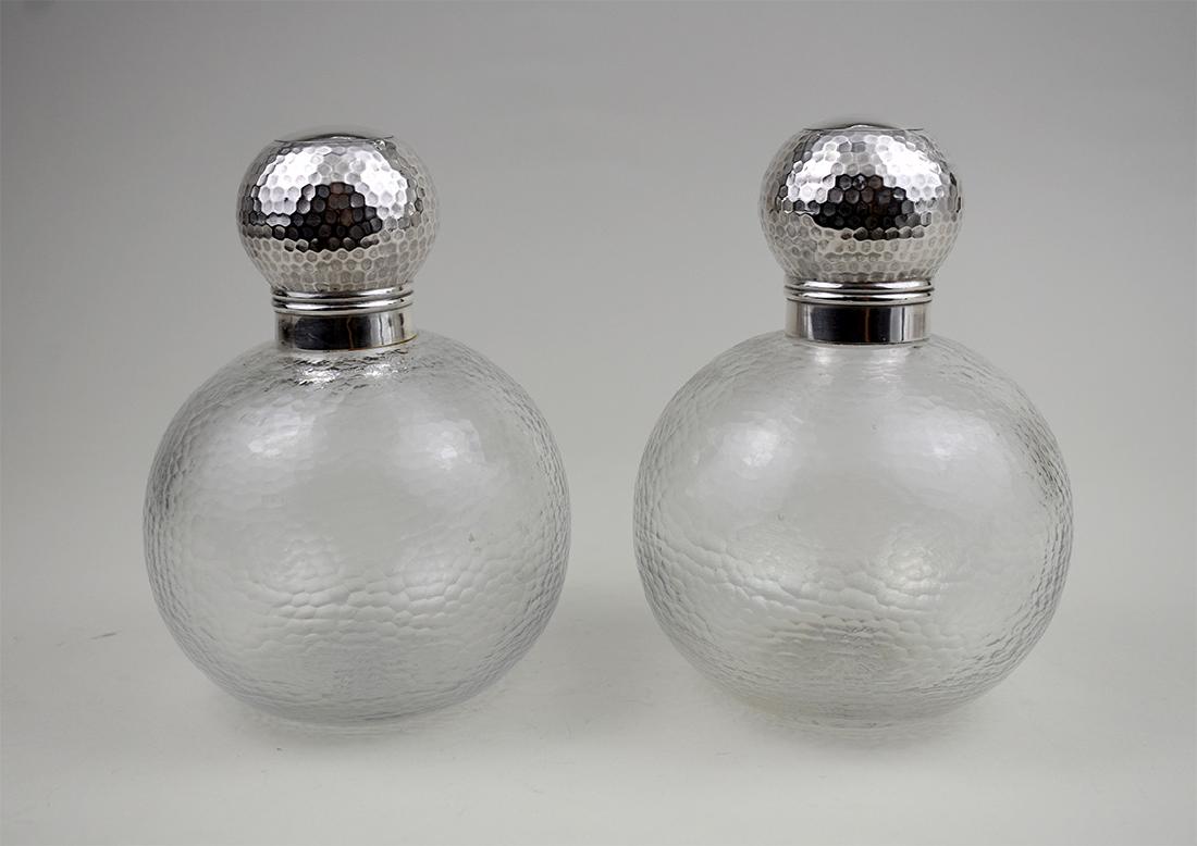 PAIR OF EDWARDIAN SILVER-MOUNTED GLASS BOTTLES: English. Late 19th/Early 20th Century. Hallmarked. Each spherical glass body with a hand-hammered texture, with hand-hammered silver caps. Height 7.50 in. Diameter 4 in. (approx) (Cond: good)