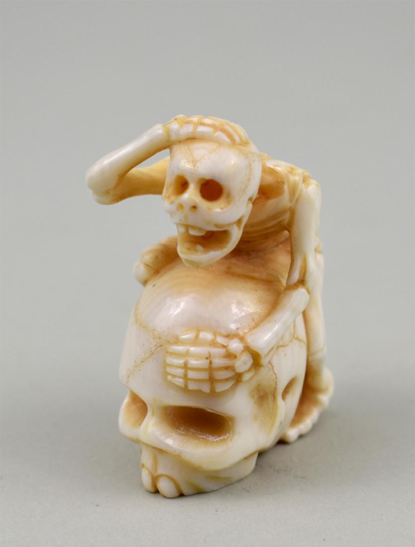 JAPANESE CARVED BONE SKELETON NETSUKE: The skeleton atop a skull. Height 1.75 in. (Cond: good)