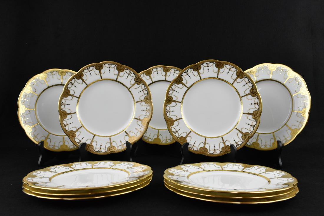 ELEVEN MINTON GILT DECORATED PORCELAIN PLATES: Early to mid 20th Century. The underside of each marked, retailed W.H. Plummer, New York. The scalloped shaped circular plates decorated around the rim with stylized textured gilt palmettos and swags.