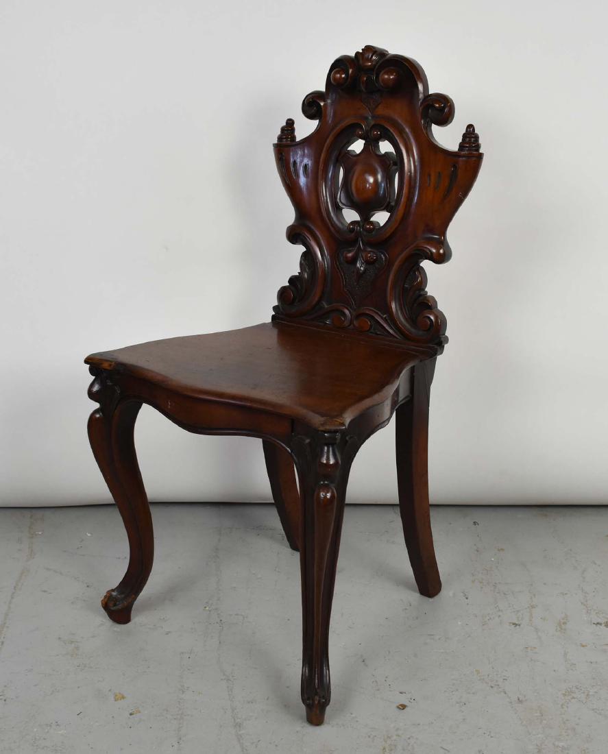 EARLY VICTORIAN MAHOGANY HALL CHAIR: Circa 1845. The solid scroll-carved back with a central cabochon cartouche, the plank seat on stylized curved legs ending in scrolled toes. (Cond: split to rear of seat)