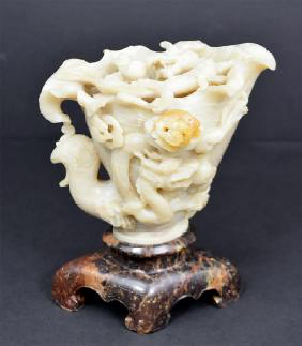 CHINESE SOAPSTONE CUP FORM DRAGON STUDY: The grayish pale green stone pierced and carved with dragons, on a carved dark soapstone base. Height 6.5 in. Width 5.5 in. (Cond: good)