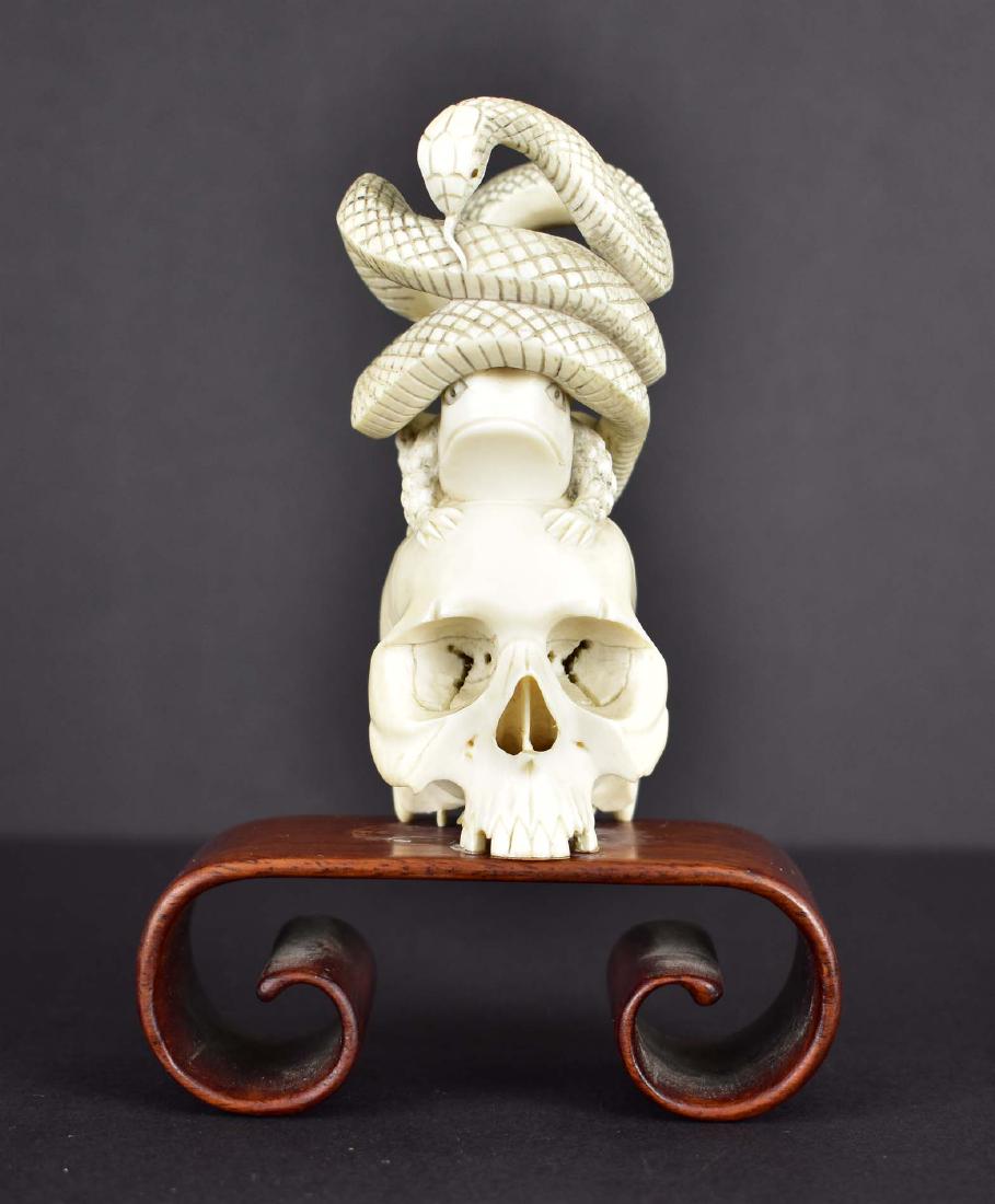 JAPANESE CARVED OKIMONO: Meiji Period, circa 1900. Depicting a serpent coiled atop a frog that sits on a human skull. Height 4.5 in. (Cond: good)