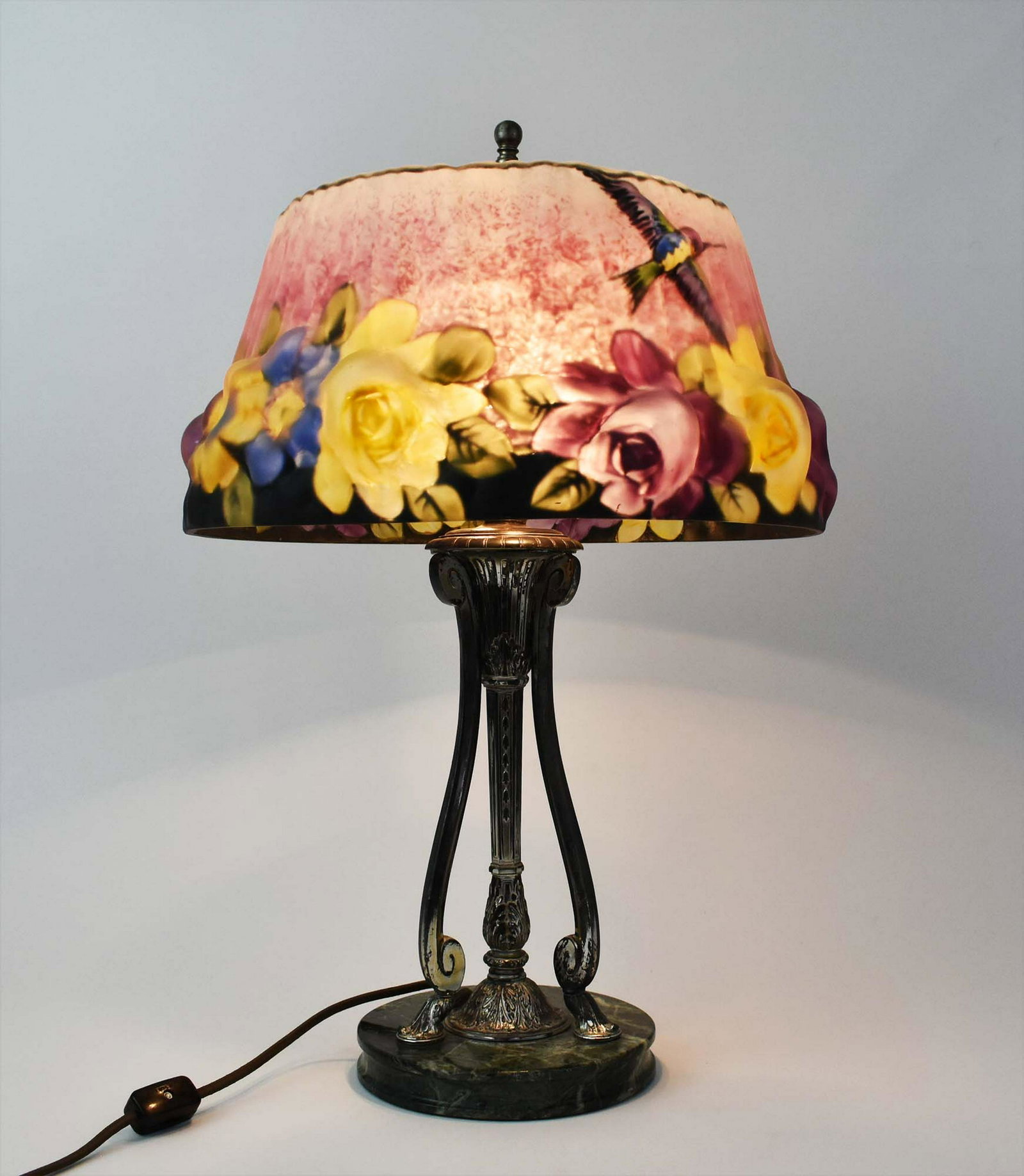 PAIRPOINT PAINTED PUFFY HUMMINGBIRD GLASS TABLE LAMP: 1900-1925. The shade marked in gilt, THE PAIRPOINT CORP. The circular Stratford shade decorated with hummingbirds in flight over colorful flowers, on a dark blue and lavender ground; the silvered meta