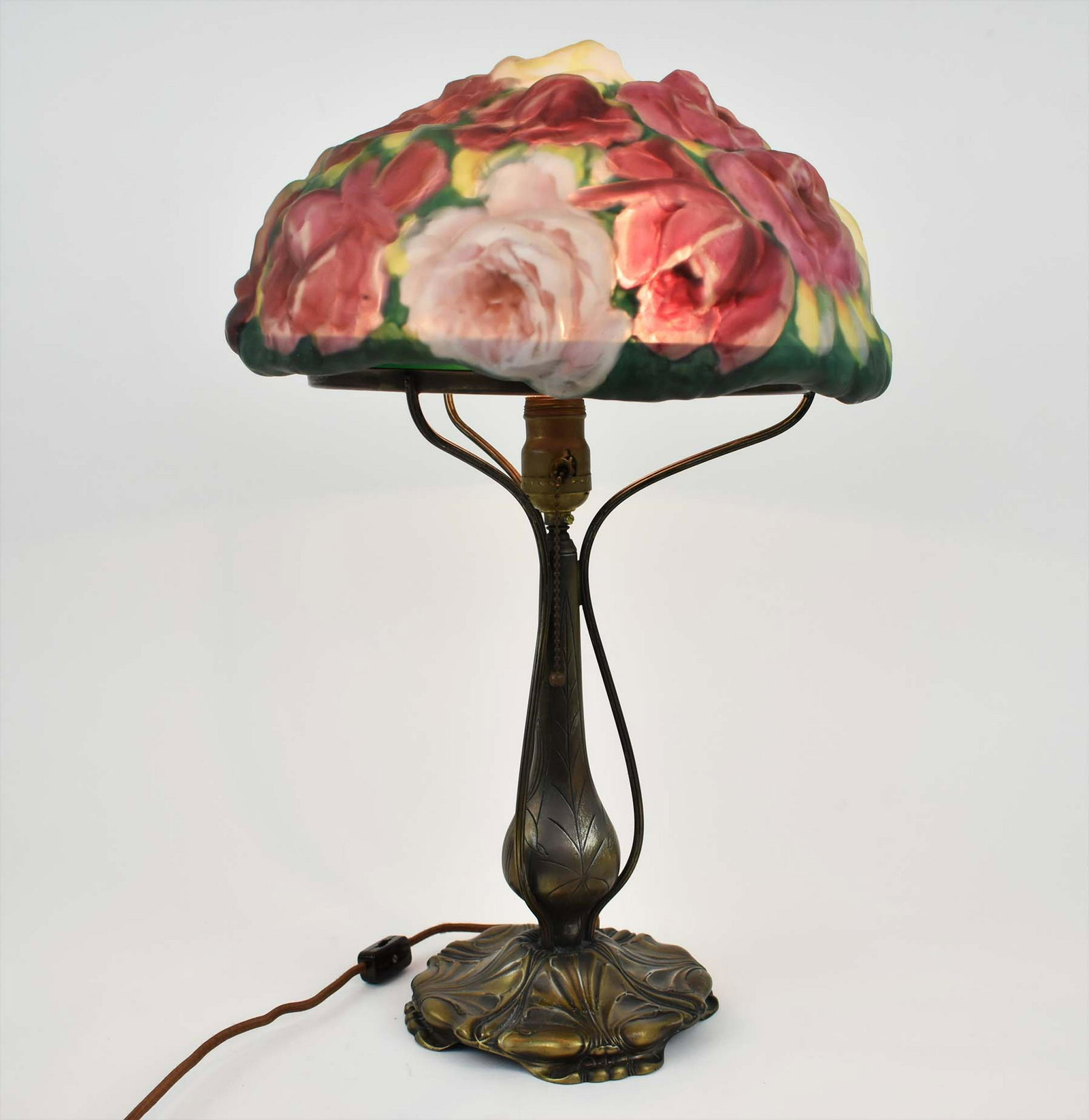 PAIRPOINT PAINTED PUFFY ROSE BOUQUET GLASS TABLE LAMP: 1900-1925. the rim marked in gilt, PATENT APPLIED 19.. The domed shaded with allover puffy roses in red, pink and white; the metal base cast with stylized leaves, faintly marked on a circular reserve,