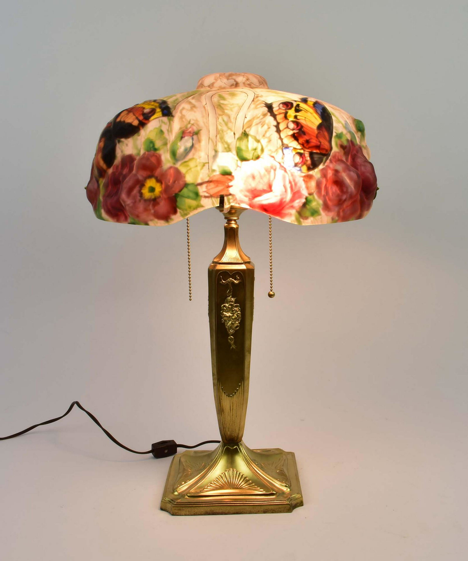 PAIRPOINT PUFFY PAINTED GLASS BUTTERFLY LAMP: 1900-1925. Unsigned. The shaped shade with a central upper dome and scalloped lower edge, reverse painted with colorful butterflies and red flower blossoms, gilt highlights, on a later two-light gilt 