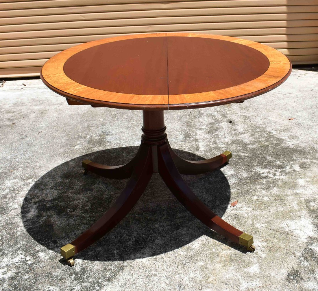 GEORGE III STYLE INLAID MAHOGANY PEDESTAL TABLE: 20th Century. Circular with a cross banded border, on a turned single pedestal, with down swept legs ending in brass feet with casters, with one leaf. Height 28 in. Diameter 48 in. Width of leaf 18 in