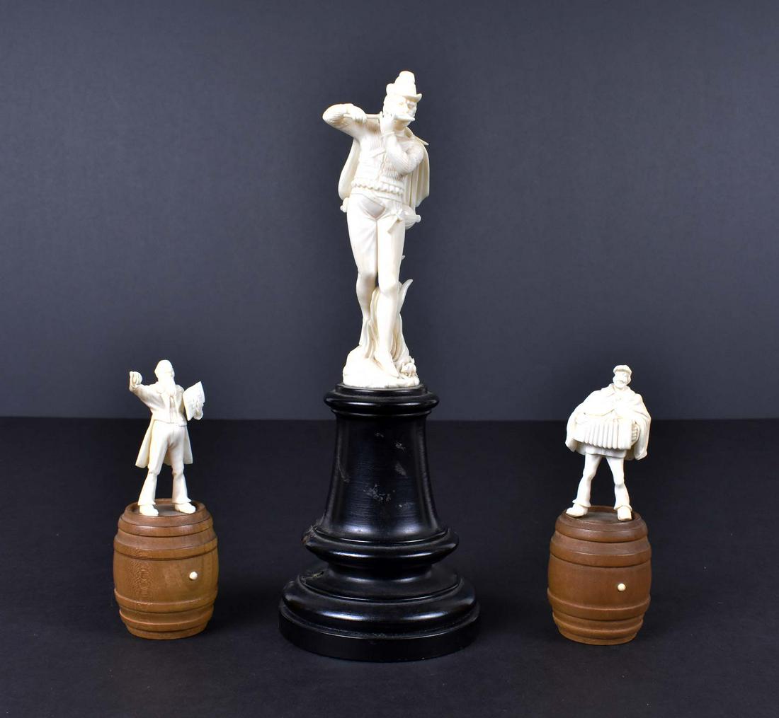 CONTINENTAL CARVED MINSTRAL & TWO FURTHER FIGURES: Late 19th Century. Austrian or German. The first plays a flute, dressed in Renaissance attire, and stands amidst long grasses, a rat by his feet, on an ebonized pedestal. The second and third depictin