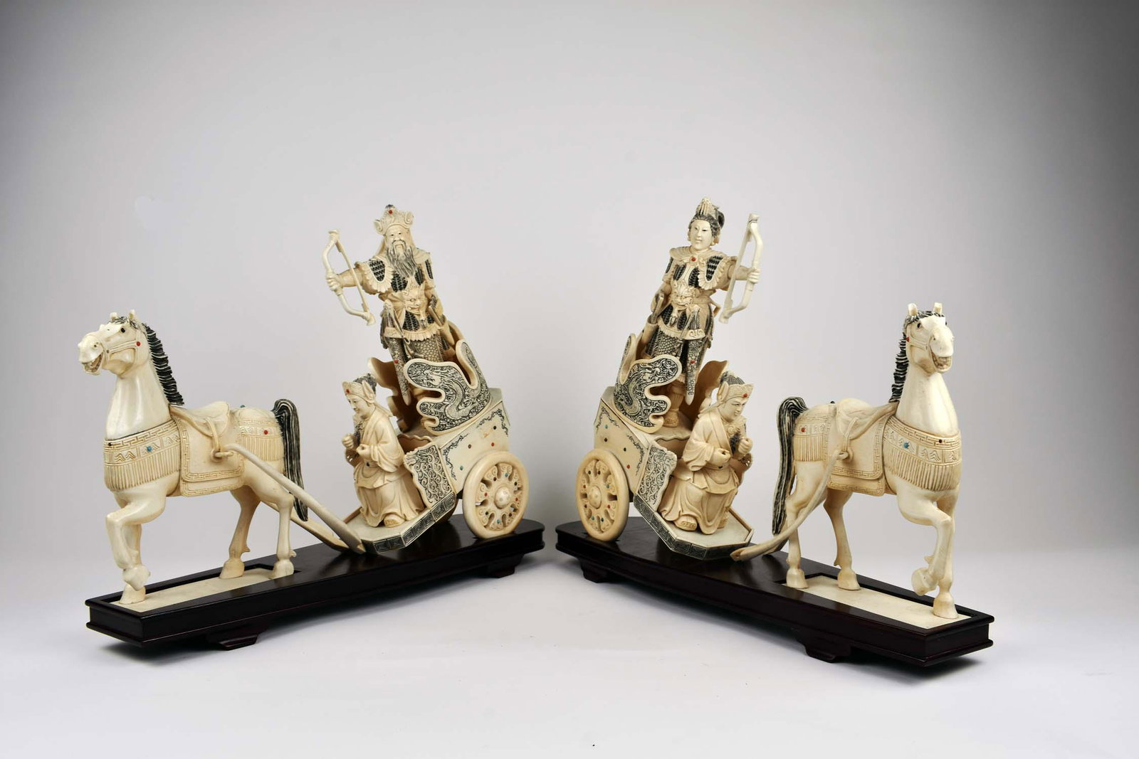 PAIR OF CHINESE JEWEL-CLAD HORSE WARRIORS IN CHARIOTS: The chariots driven by figures with arches in robes clad in full armor behind, set on wood bases. Height of chariots and archers 14.5 in. Horses 9.5 in. Width overall 18.5 in. Depth 4.5 in. (Cond: goo