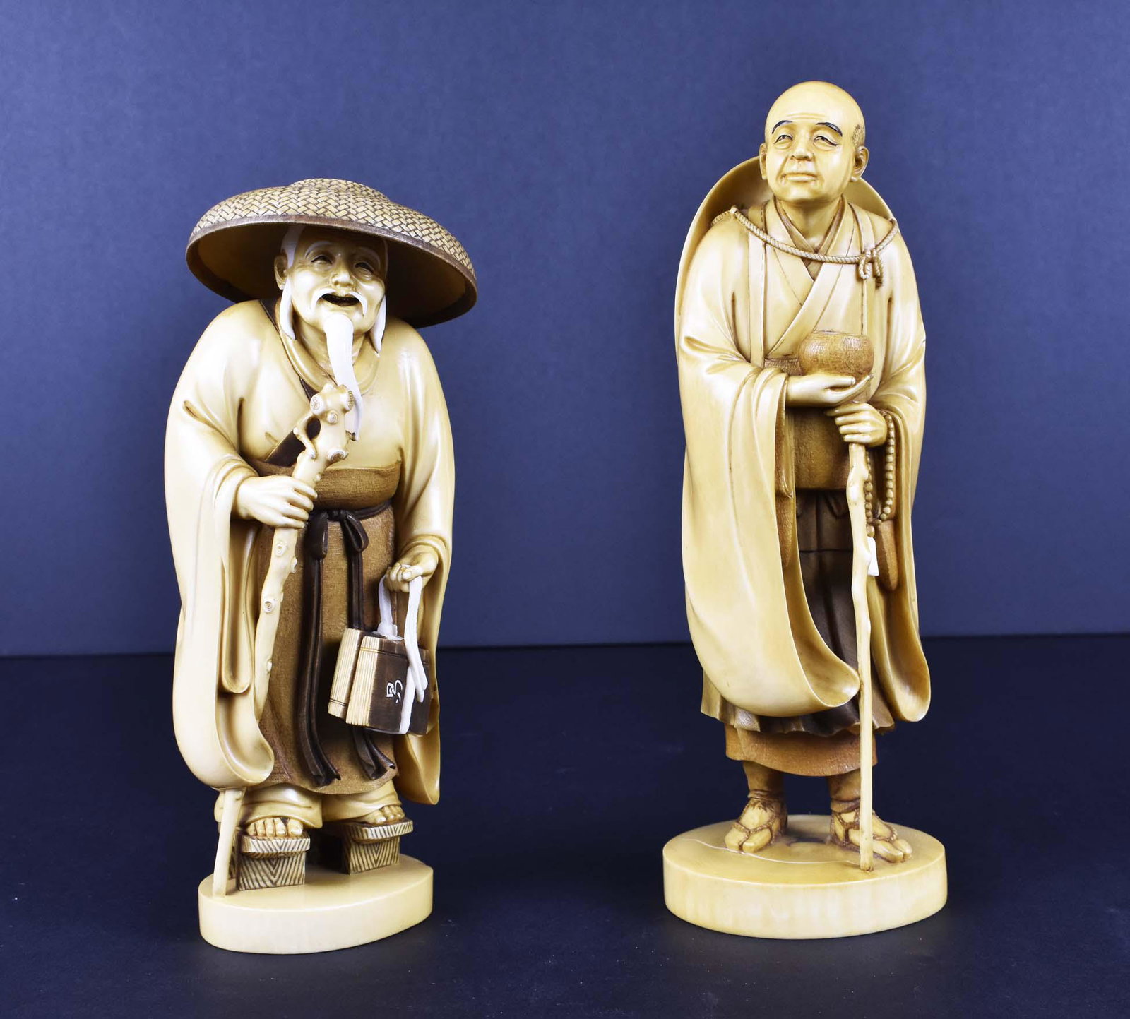 TWO JAPANESE OKIMONO OF A PRIEST AND A POET: Meiji Period. The priest, signed Ryudo, with an alms bowl and his staff, the poet, Signed Gyokusho, in a sedge hat carrying two books. Heights 8.75 in., 7.25 in., respectively. (Cond: good)
