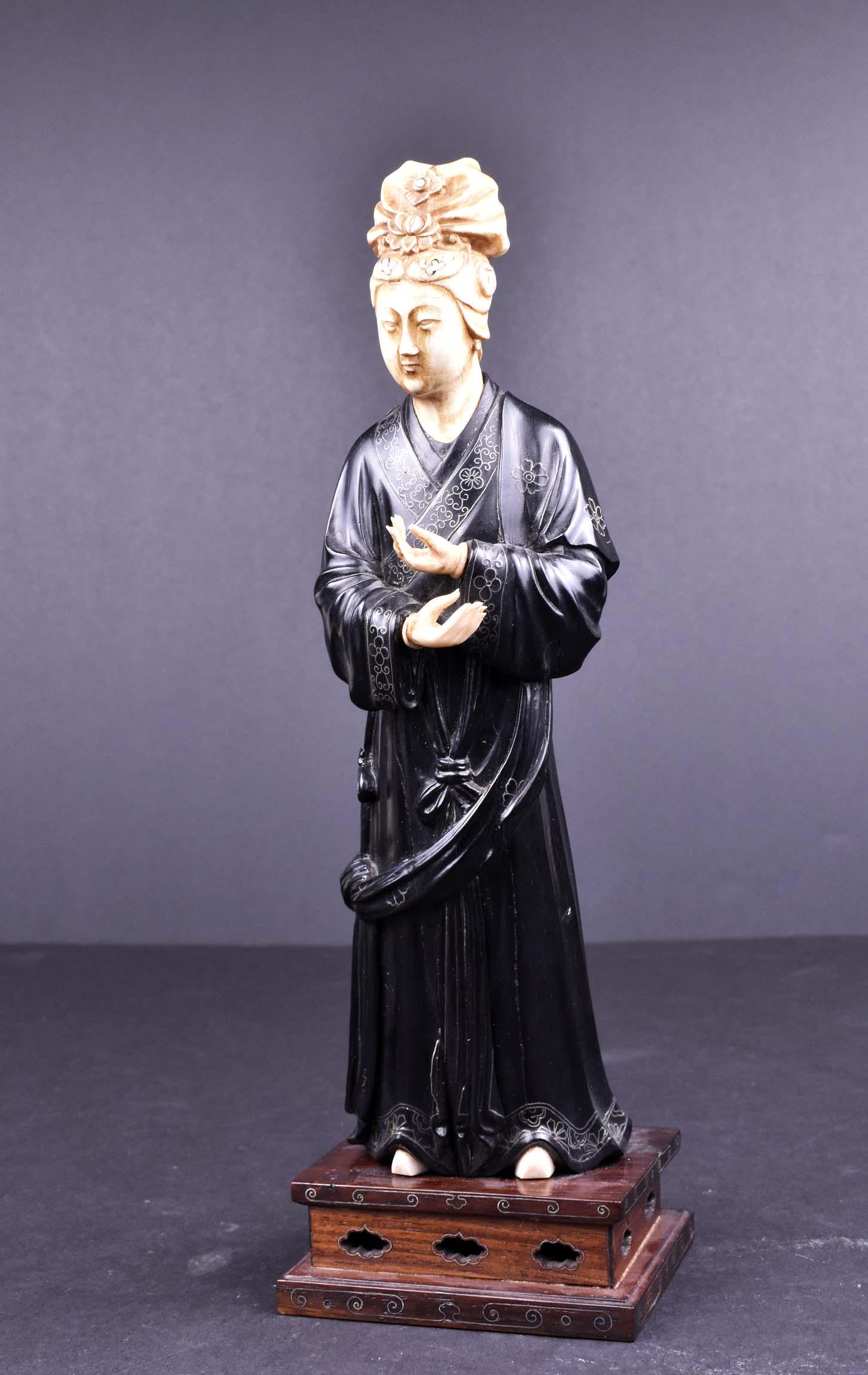 UNUSUAL CHINESE CARVED FIGURE OF ELEGANT MAIDEN: Ching Dynasty, 19th Century. Dressed in a black stained long robe, her hair well coiffed and set with inlaid mother-of-pearl devices, on a wood stand. Height 10 in. (Cond: good)