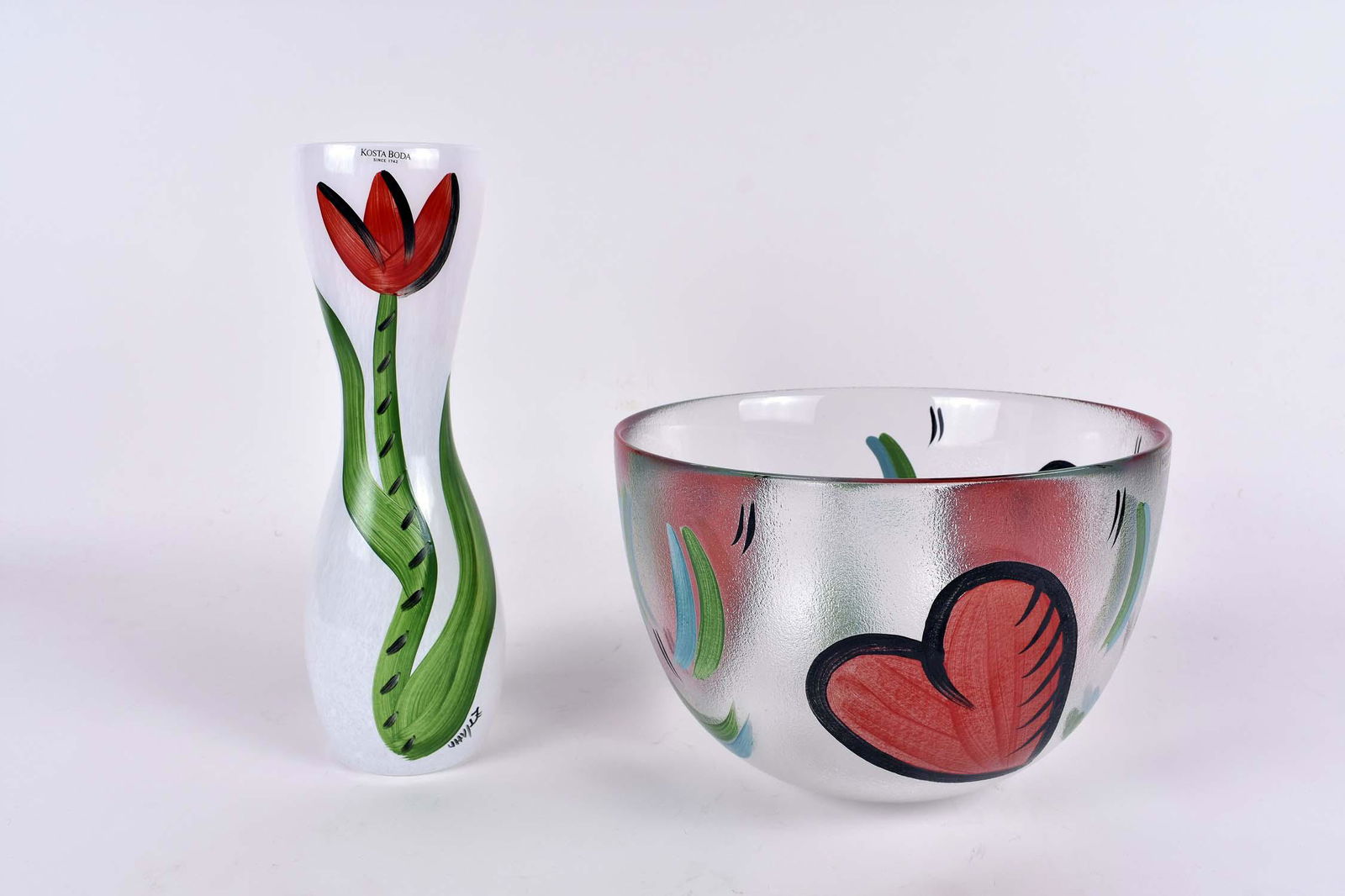 TWO CONTEMPORARY KOSTA BODA PAINTED GLASS VESSELS: Ulrica Hydman â€“Vallien. Signed, and with Kosta Boda applied label. The first a bowl decorated in red and green with hearts; the second, a vase, painted with a tulip stem on a white internally d