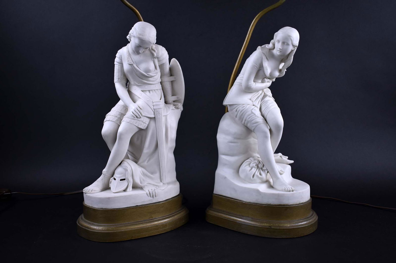 PAIR OF ENGLISH PARIAN WARE FIGURAL TABLE LAMPS: Applied factory and registry seal, John Bell. The female seated upon a rock, depicting a traveler and a warrior, on a wood base. Height of figures 14 in., overall 23 in. (Cond: good, electrified)