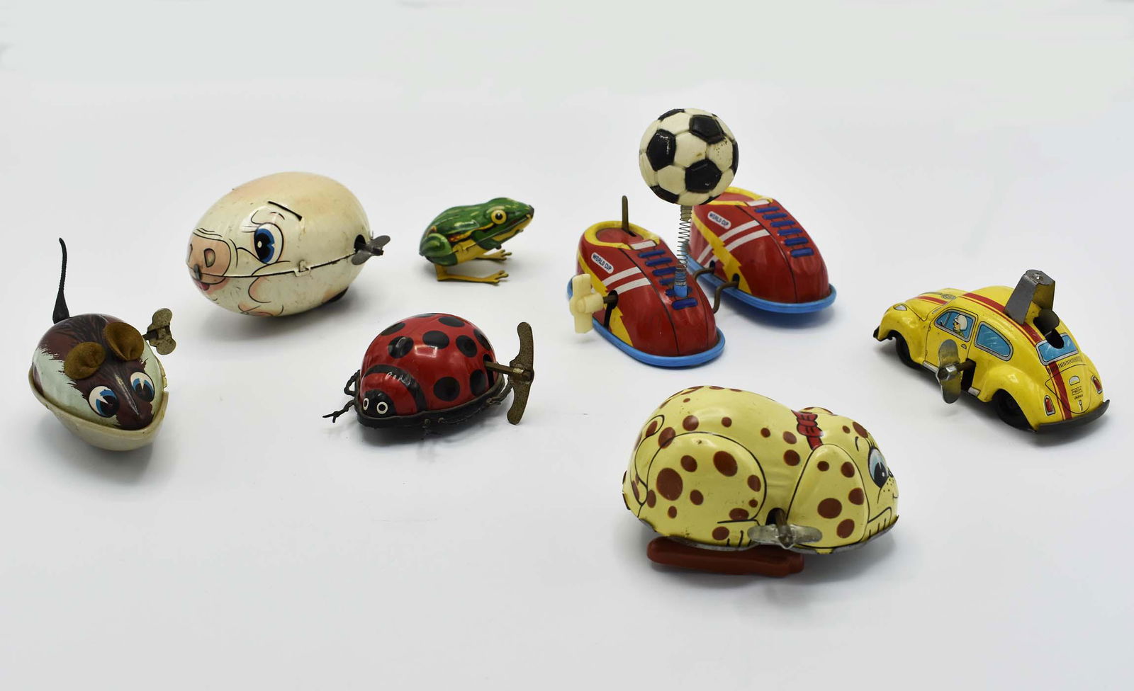 SEVEN VINTAGE VARIOUS PAINTED TIN WIND UP TOYS: 1930â€™S to 1940â€™S. Comprising: a Japanese, Yone piglet and a puppy, both marked; a Japanese Endoh yellow Volkswagen, marked; a pair of sneakers with a soccer ball, also Japanese; a West G