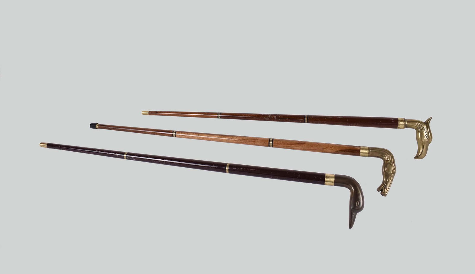 THREE PORTABLE BRASS-MOUNTED ANIMAL HEAD CANES: Continental. Comprising: an eagle headed example, a horse-headed example and an example with a duckâ€™s head, all with mahogany or hardwood shafts. Length 35 in. (Cond: good)