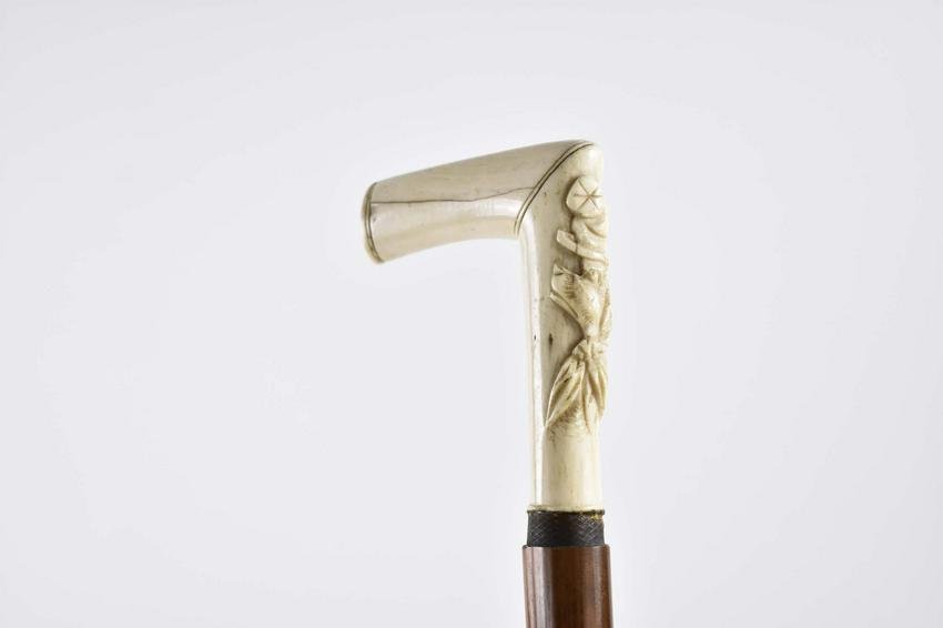 AMERICAN FOLK ART CARVED BONE & MALACCA WALKING STICK: Second Quarter 19th Century. By repute previously one of Daniel Websters walking sticks. The bone handle whimsically carved in relief with the head of a hound, wearing a knotted scarf and hat, above a