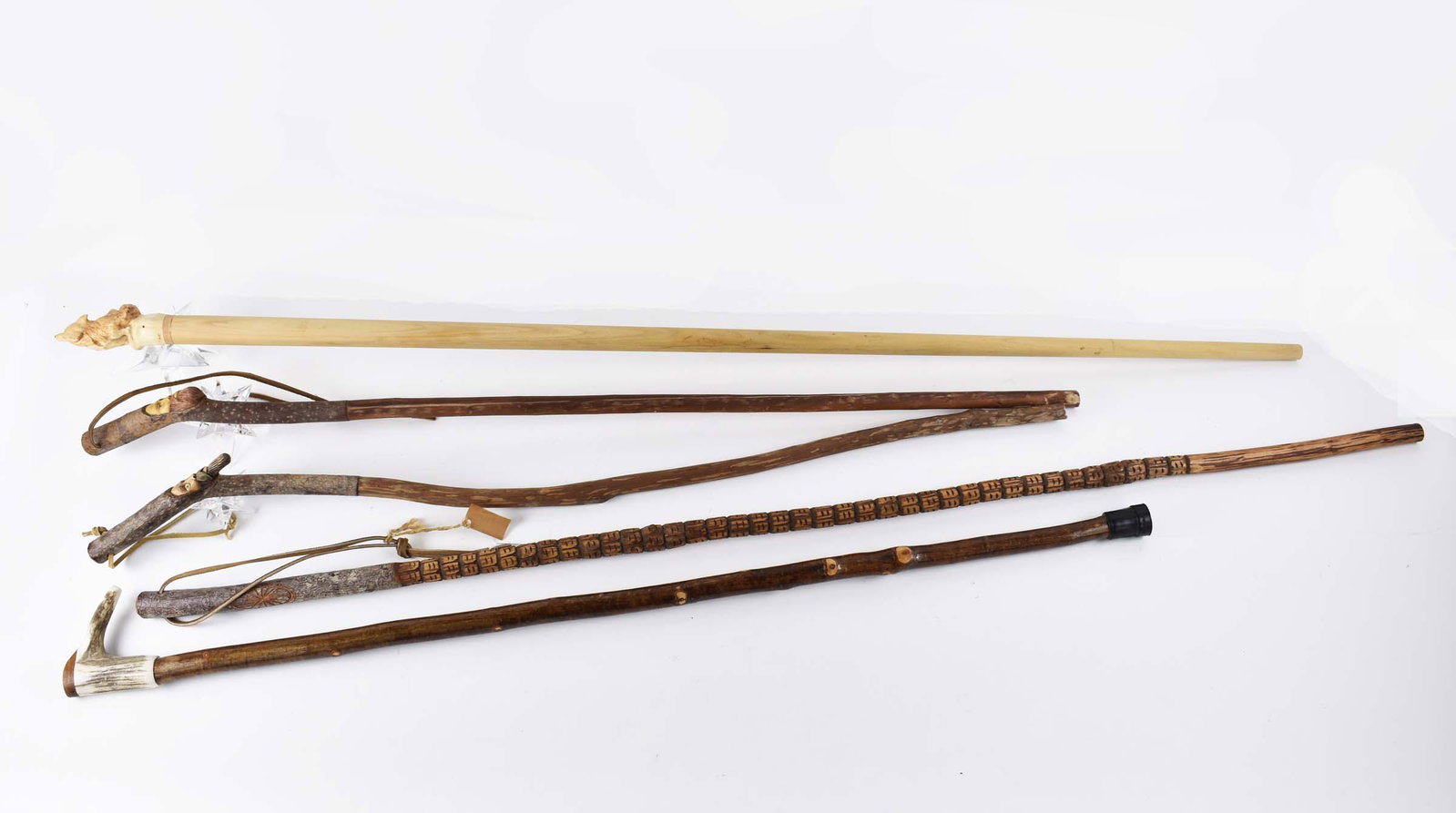FIVE VARIOUSLY CARVED WOOD HIKING STAFFS: Most Continental. Comprising: an example with a turned tapered shaft headed by a carved howling wolf; a natural branch with antler handle carved as a whistle; a third, with a handle partially carved w