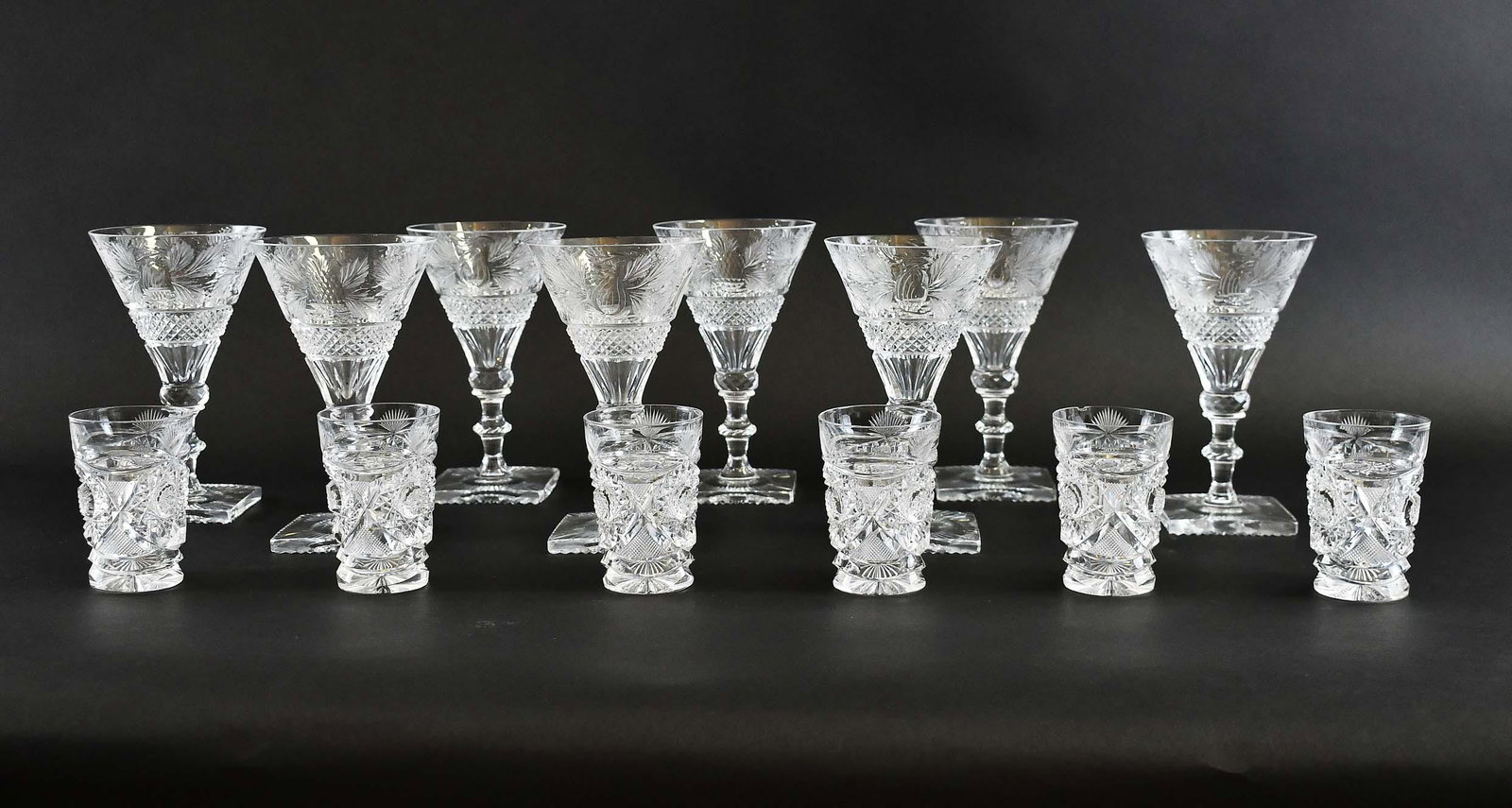 SIXTEEN ENGLISH CUT-GLASS DRINKS GLASSES: 20th Century. Comprising a set of eight wine glasses, with cone-shaped bowls on knoped stems with square bases, the bowls cut with a wide band of leaves above a diamond pattern, with two further cylin