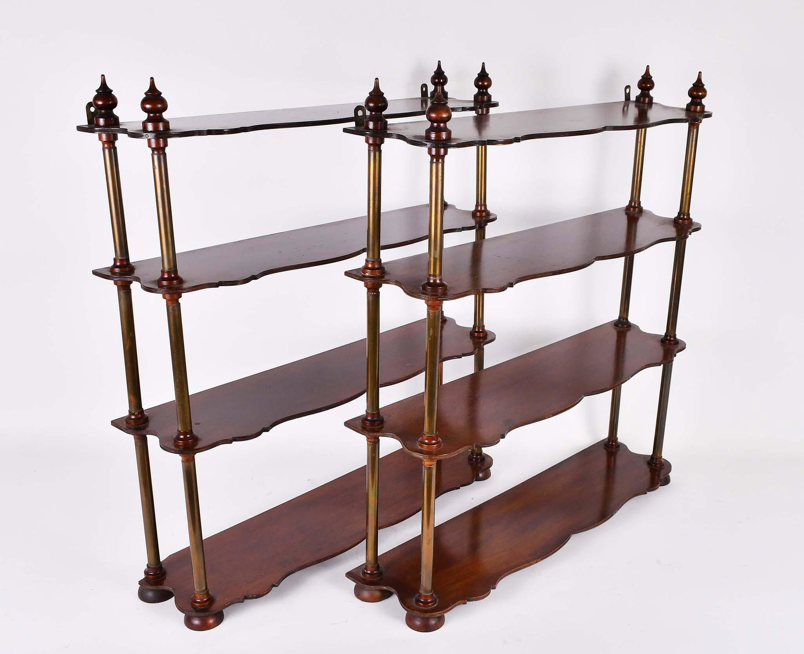 PAIR OF BRASS-BOUND MAHOGANY WALL SHELVES: In a George III style. The four shaped shelves with either brass supports or treen finials. Height 24 in. Width 23.5 in. Depth 5.5 in. (Cond: small piece from one lower rear shelf lacking)