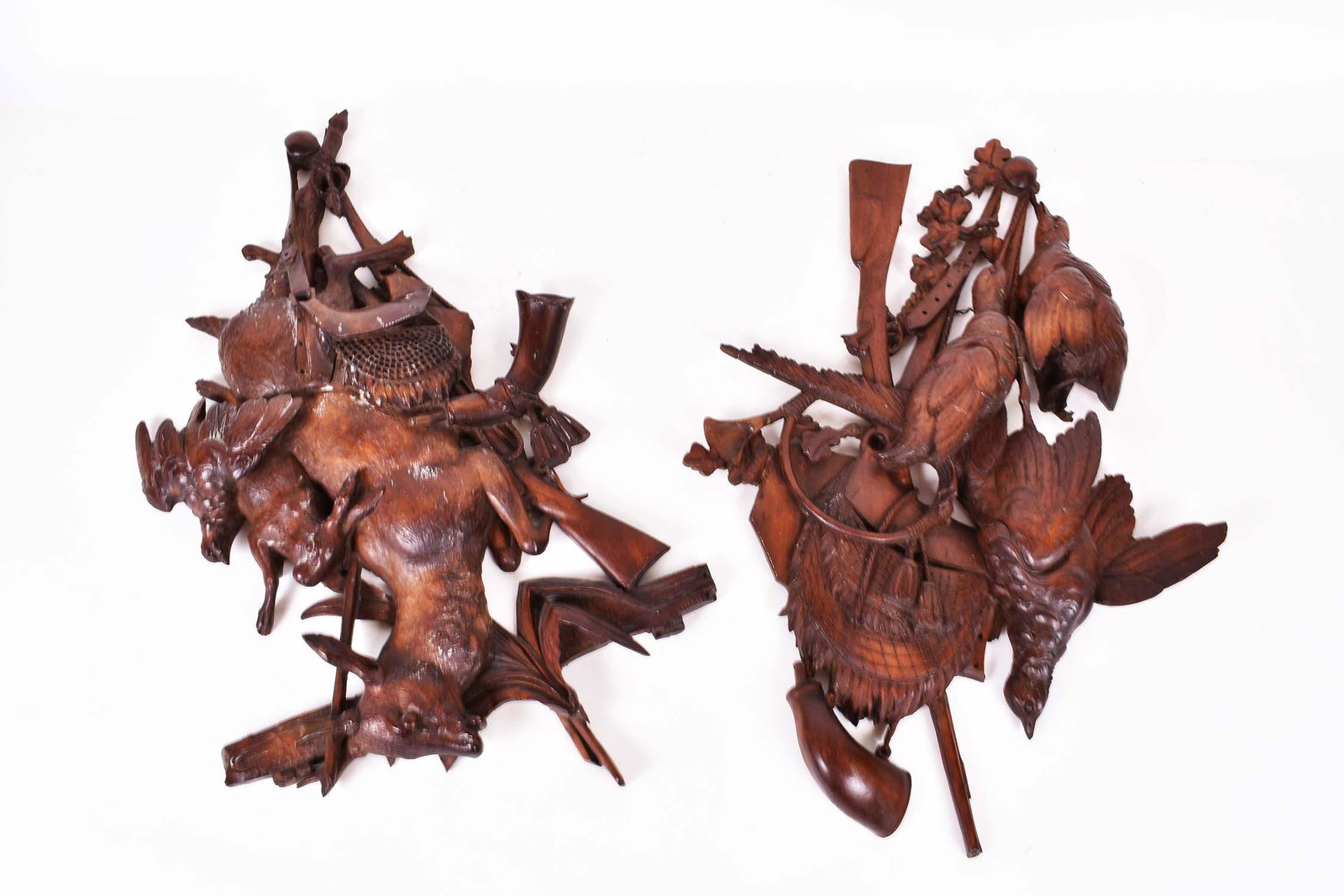 PAIR OF GERMAN CARVED WALNUT HUNTING TROPHY PLAQUES: Late 19th/Early 20th Century. South German or Tyrolean. Both heavily carved in high relief, one depicting a deer with rabbit and a pheasant, with a rifle, powder horn and bag; the other with three phe