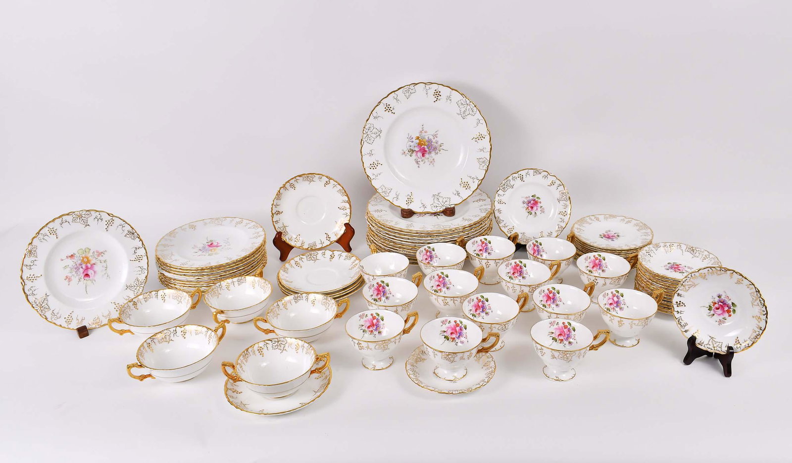 ROYAL CROWN DERBY 74 PIECE PORCELAIN DINNER SERVICE: First Half 20th Century. Each piece marked. In the Vine pattern. Each molded circular piece with a parcel gilt edge, the center recess with a floral bouquet. Comprising: 12 dinner plates, 11 luncheon 