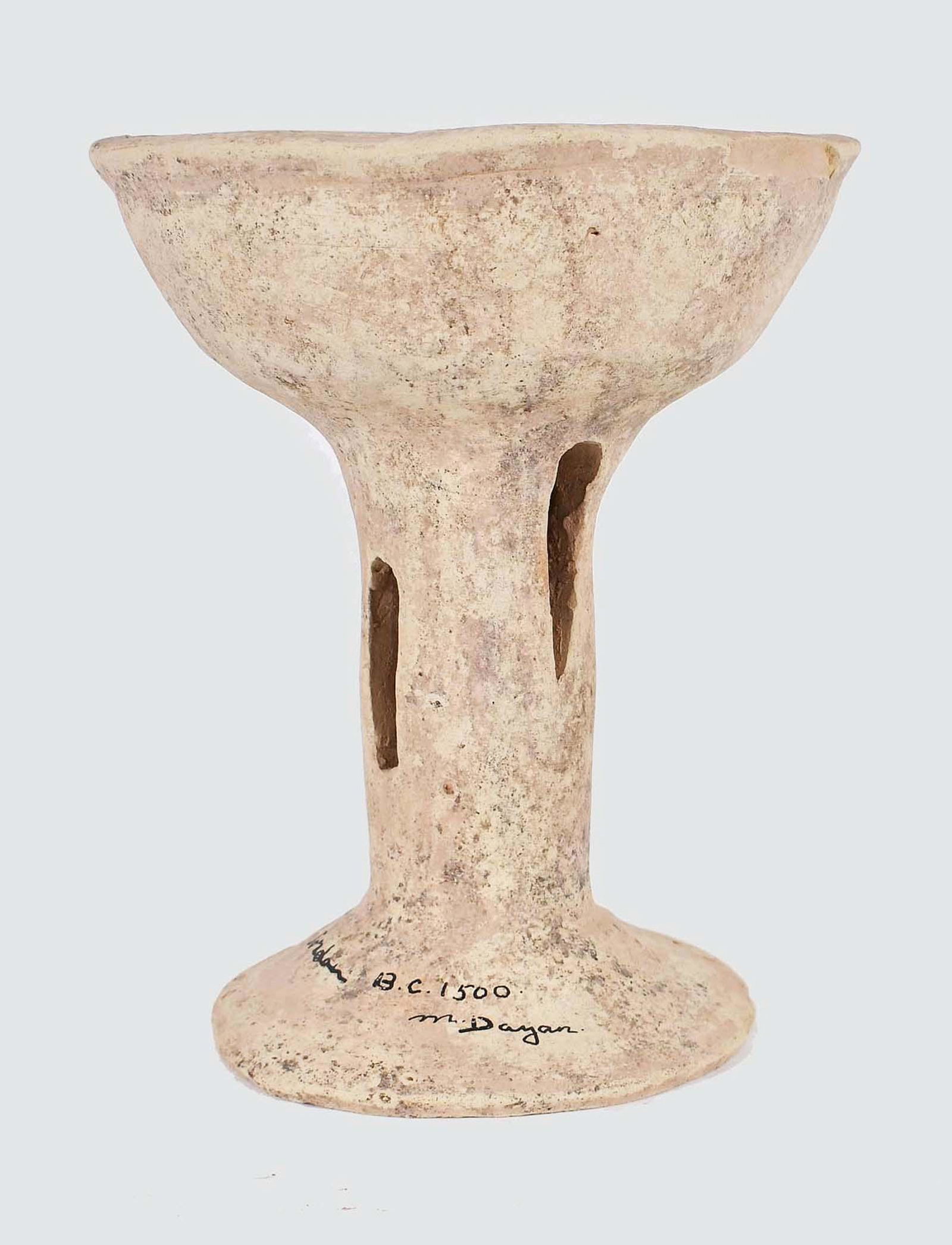LATE BRONZE AGE TERRA COTTA CHALICE: Jordan, 1500 B.C.E. Signed M. Dayan, Jordan, 1500 BC. The cream-colored earthenware chalice with a tapering dish shaped bowl above a cylindrical shaft pierced with a wide slit, on a circular spreading