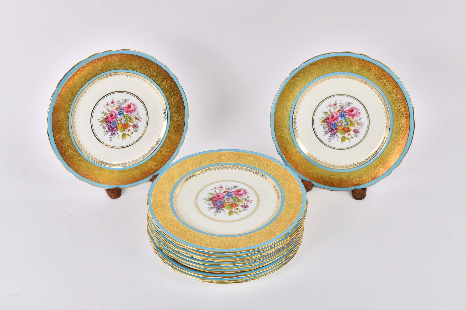 12 AYNSLEY PAINTED & GILT EARTHENWARE SERVICE PLATES: English. First Half 20th Century. The undersides marked. Each scalloped rim with an inner and outer powder blue band centering a wide textured gilt band chased with foliage, the center recess painted 
