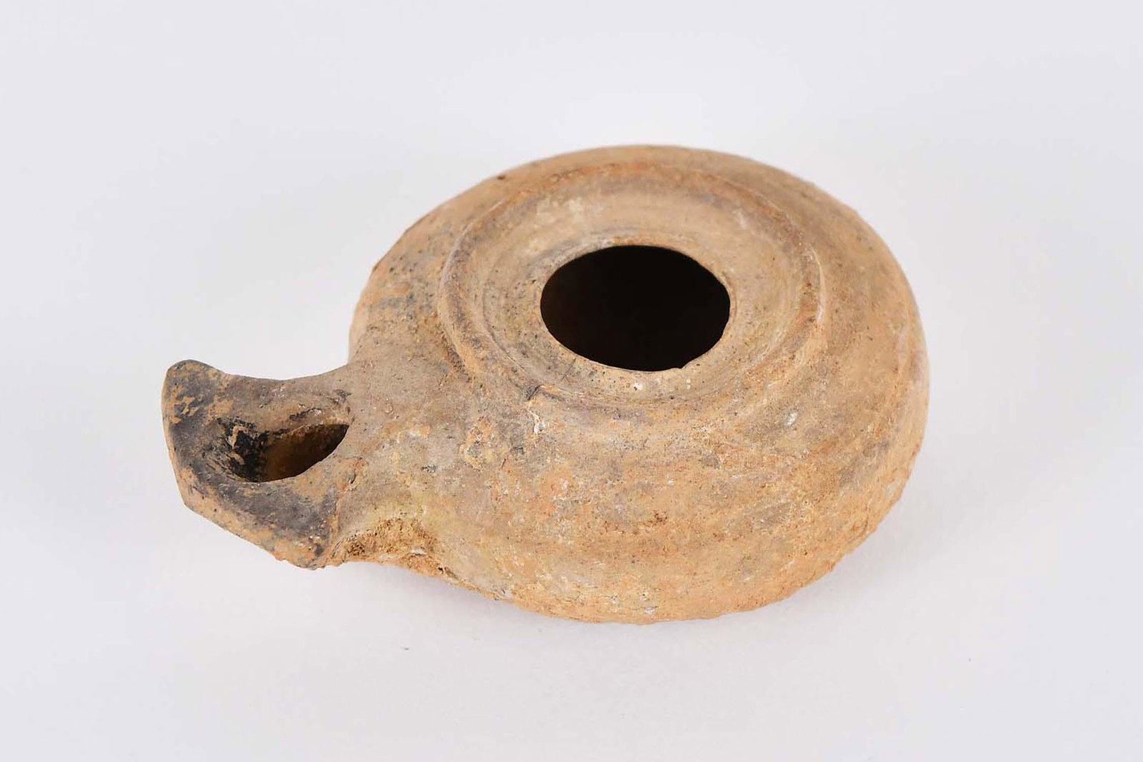 HELLENISTIC / ROMAN PERIOD TERRA COTTA OIL LAMP: 300 B.C.E. to 300 A.D. Circular with a pierced center and projecting shaped spout. Length 3 in. Diameter 2.25 in. Provenance: The Collection of Erwin and Sylvia Harvith, Detroit, MI, acquired in 1972