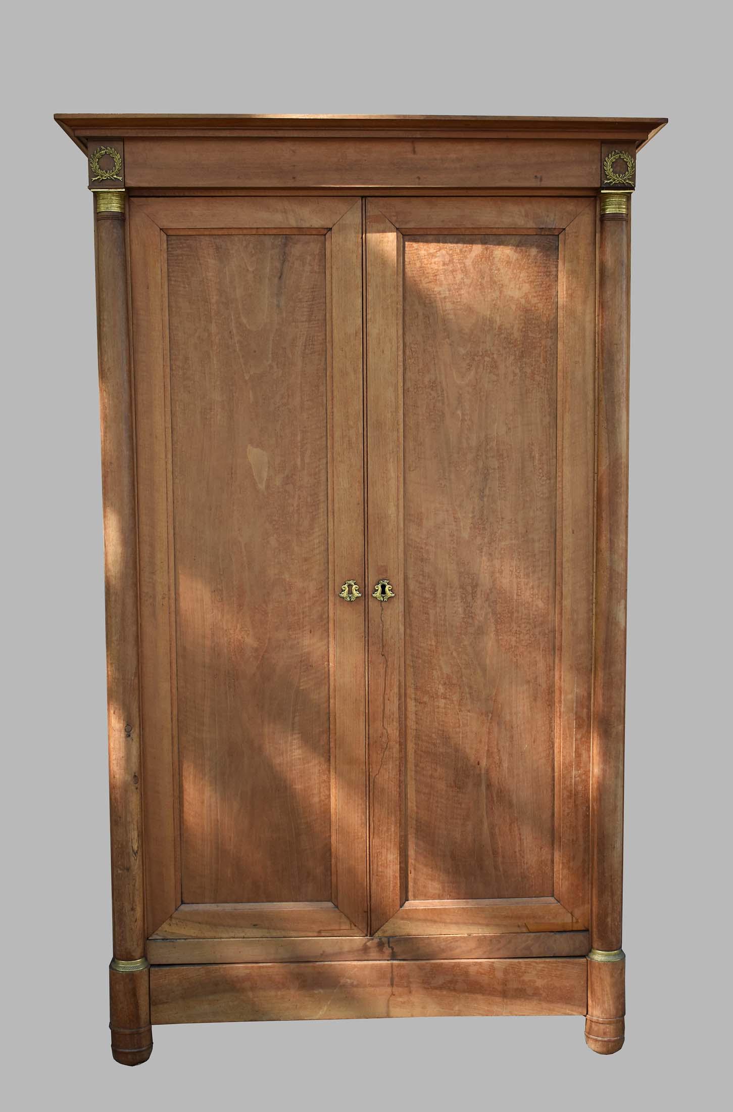 CHARLES X BRASS-MOUNTED MAHOGANY ARMOIRE: Circa 1830. The flattened cornice above two paneled doors, flanked by half columns, capped and ending with gilt bronze collars, raised on shaped bun feet. Height 6 ft. 9 in. Width 4ft. 3 in. Depth 25 